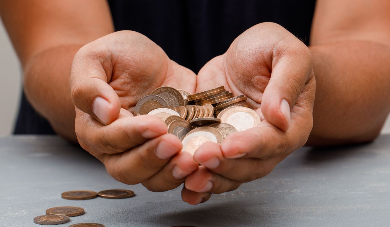 Imagem mostra duas mãos segurando moedas