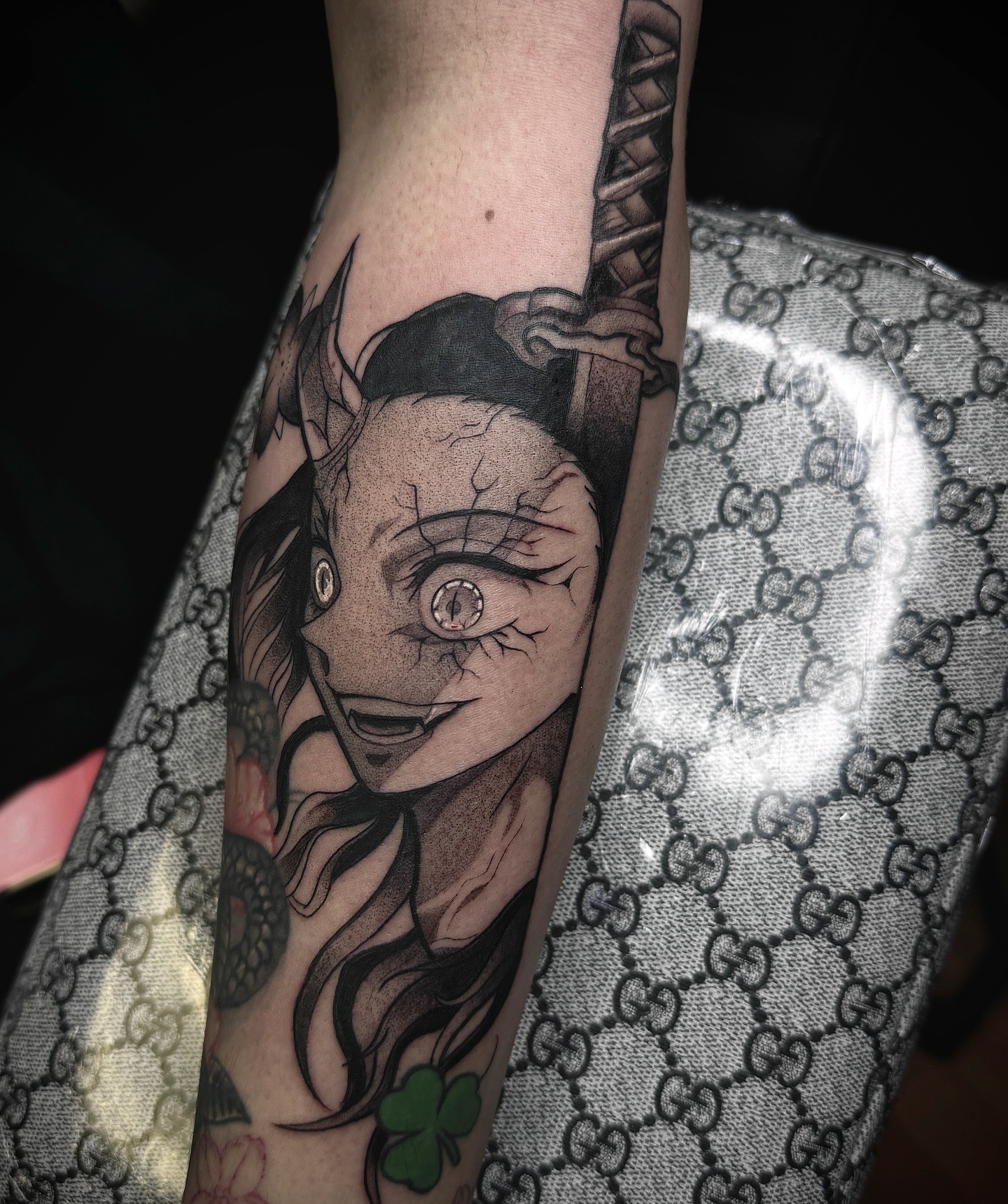A grayscale anime-style tattoo of a character with spiky hair and a headband, holding a kunai.  The tattoo is on someone's forearm.