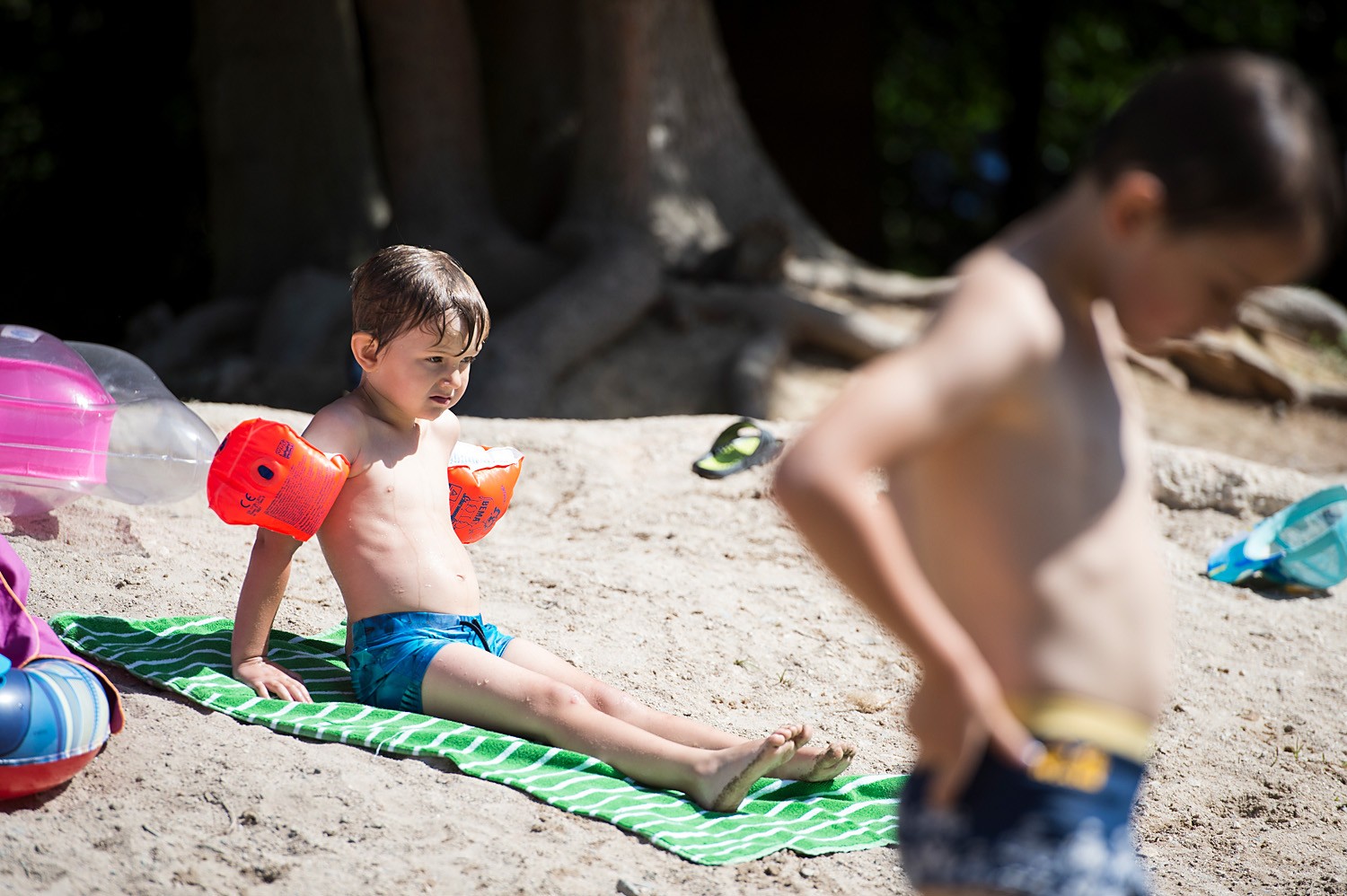 Kind mit Schwimmärmeln liegt auf einem Handtuch am Sandstrand 