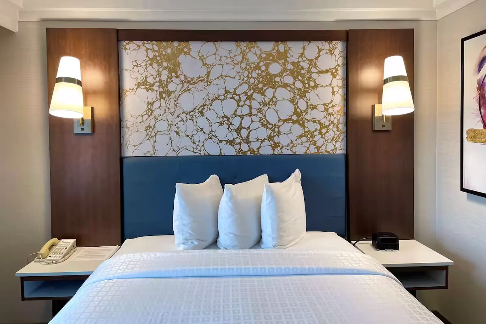 Hotel room with a bed, blue headboard, and gold marbled accent wall.