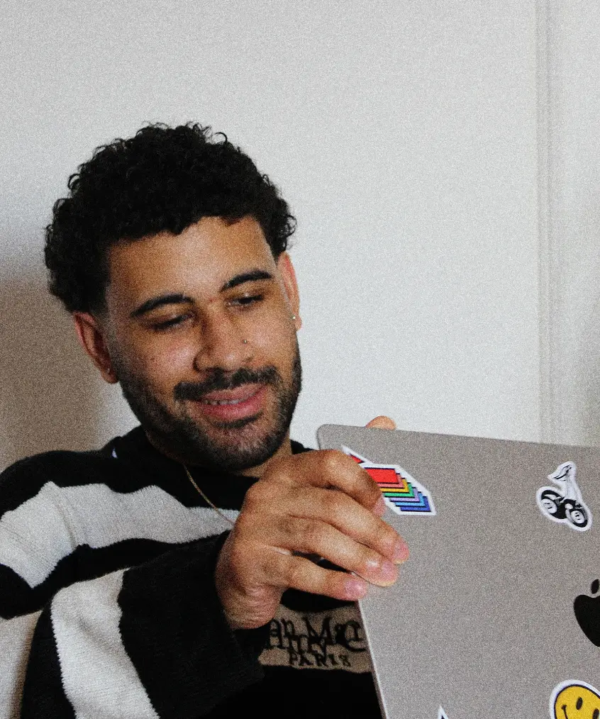 Casual portrait of Karim smiling while holding a laptop covered in creative stickers.