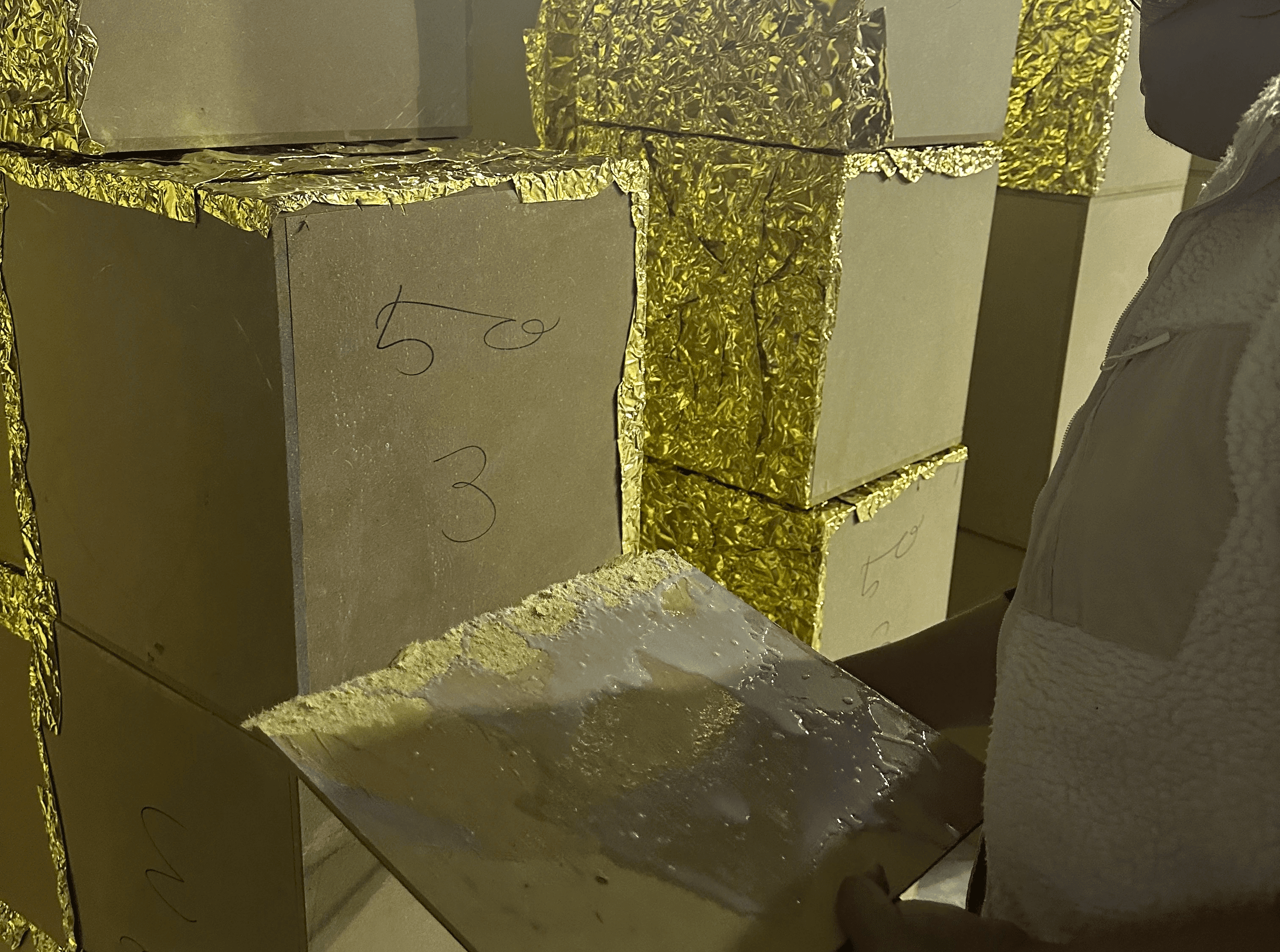 작업장에서 진행 중인 대형 골드 큐브 조형물 제작, 금박 시트 접착 / Large-scale gold cube sculpture fabrication in workshop, gold foil application