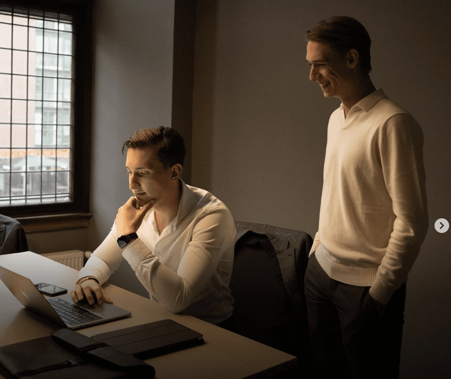 Four diverse professionals collaboratively working on a laptop, with one person pointing at the screen while others observe.