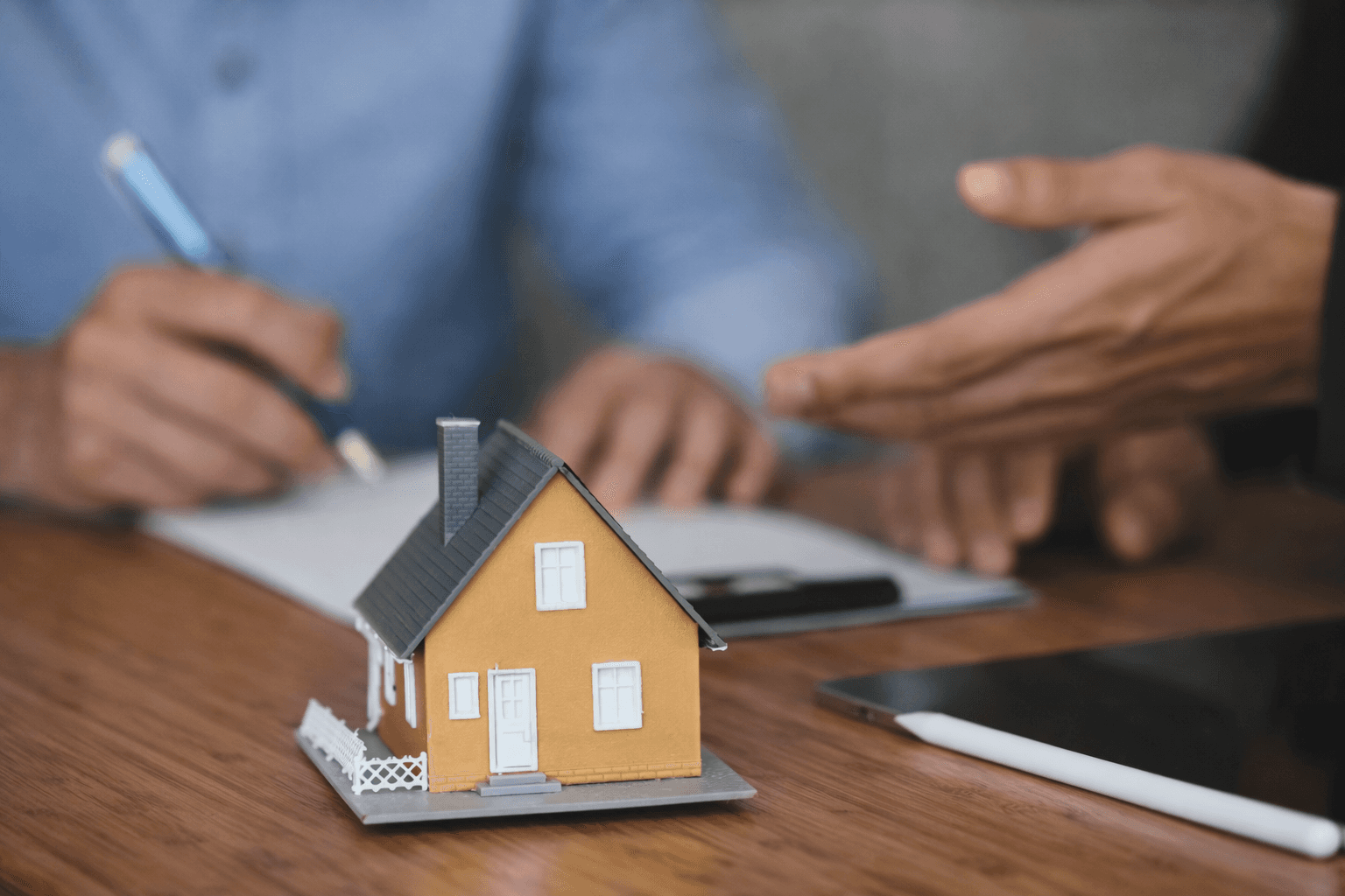 Small model house on a table while people review and sign housing documents.