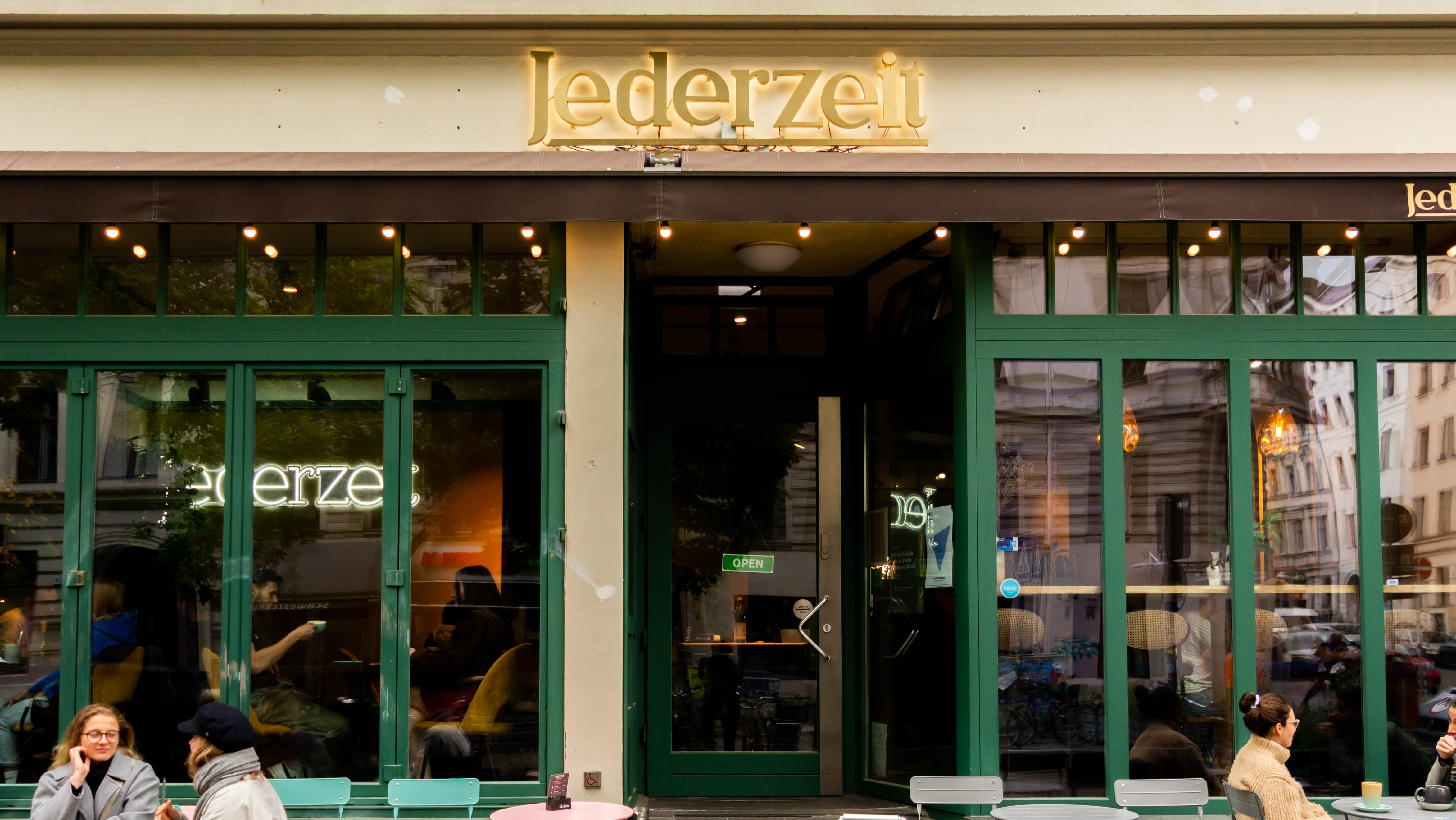 A cozy cafe exterior with green doors and large windows, inviting patrons to enjoy a warm atmosphere.