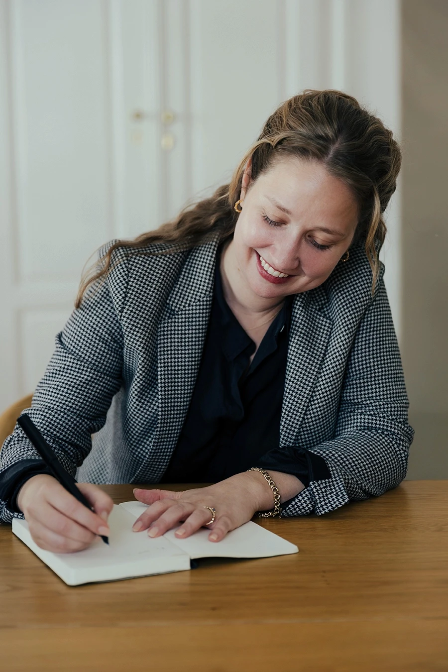 Lindsay E. Lynch, editor and writer at Sense and Syntax, smiling while writing notes in a notebook during a work session.