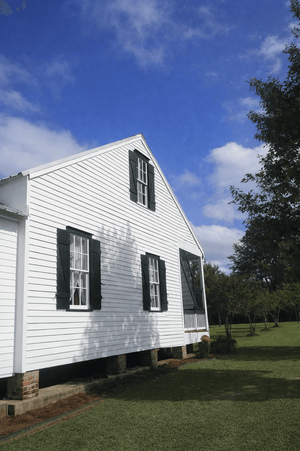 A modern, luxury beachfront villa with large glass windows and balconies overlooks a rocky shoreline, surrounded by palm trees at sunset.