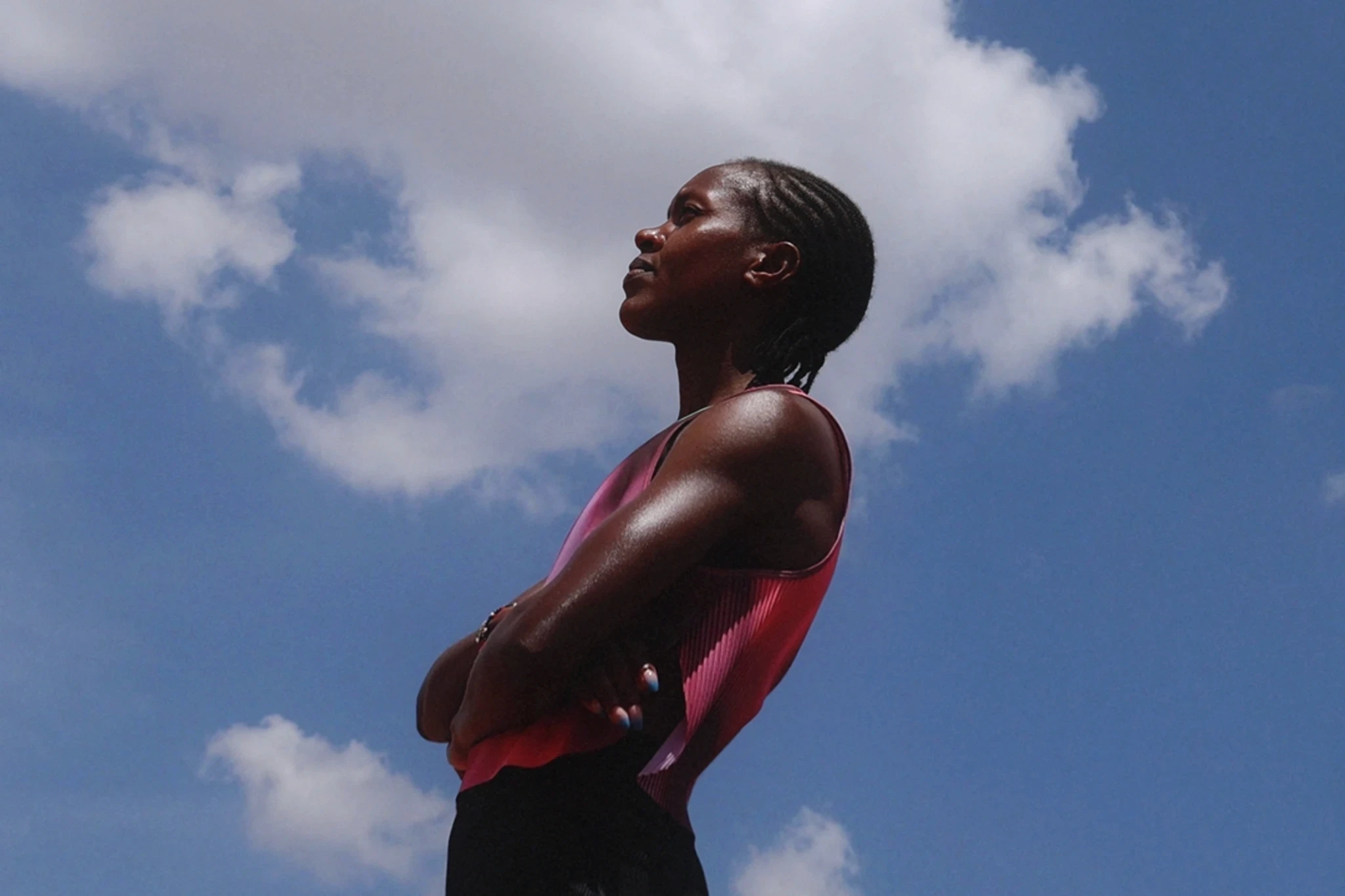 Faith Kipyegon with her arms crossed looking up at a bright blue sky