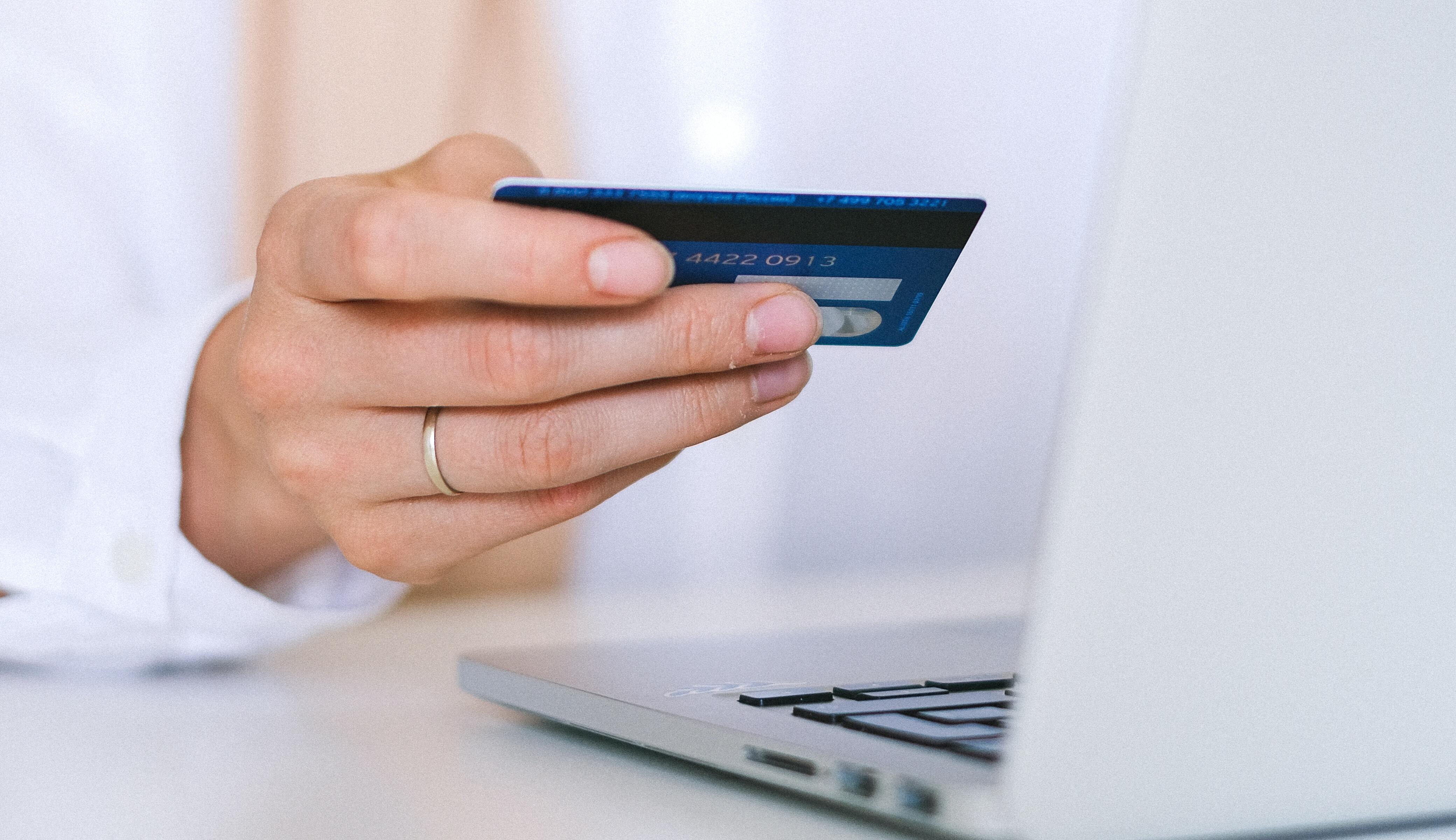 Een hand houdt een creditcard vast bij een laptop, wat online winkelen of betalingsverwerking suggereert.