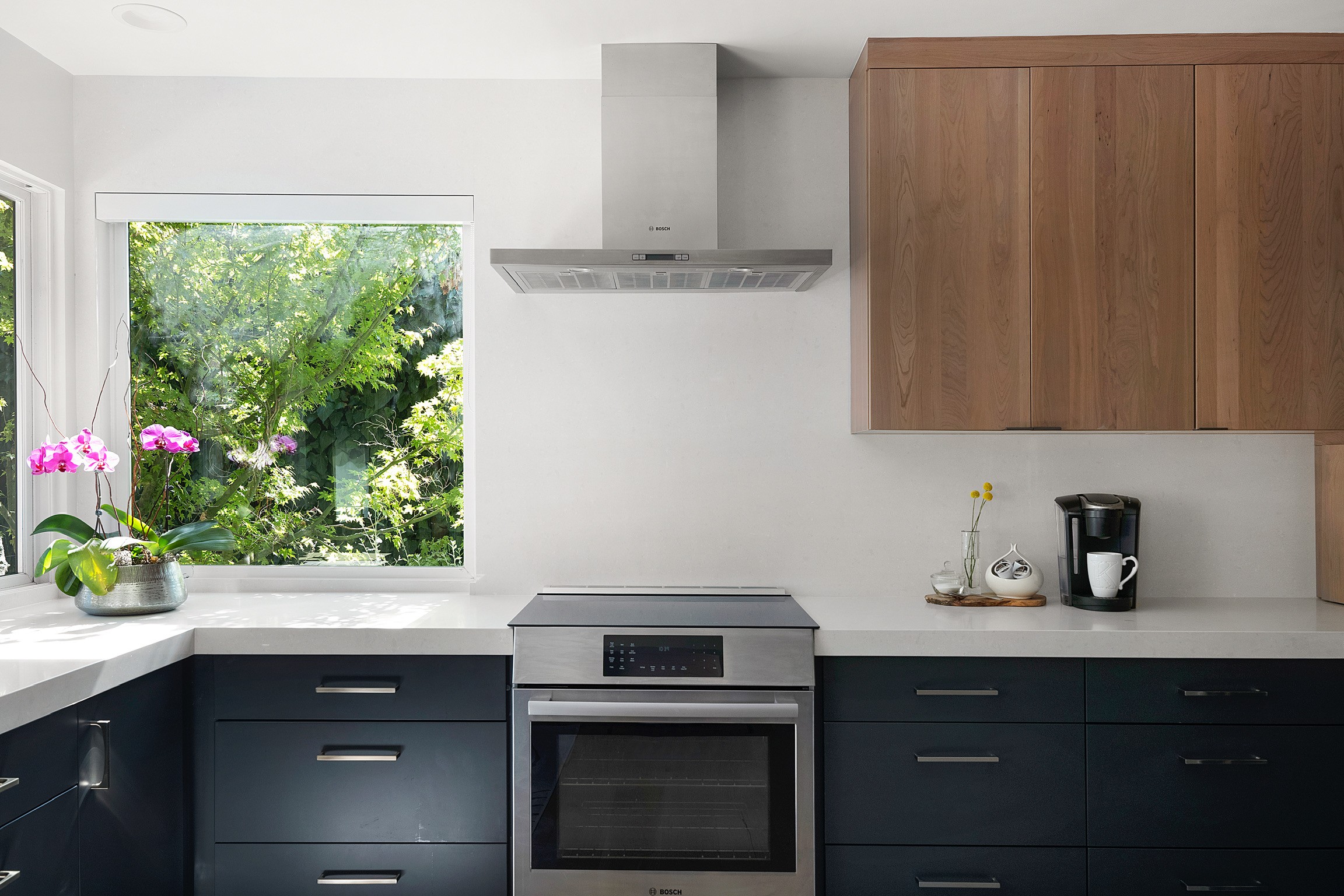 “Contemporary kitchen with dark blue cabinets, white countertops, and large window over the sink”