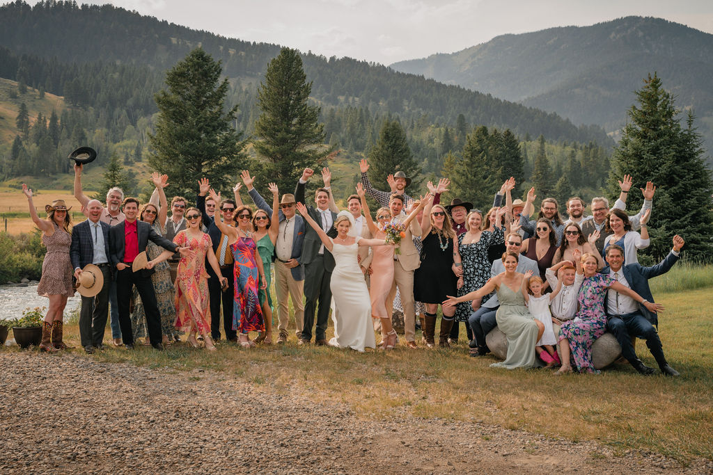 Newlyweds posing with wedding guests in a mountain meadow