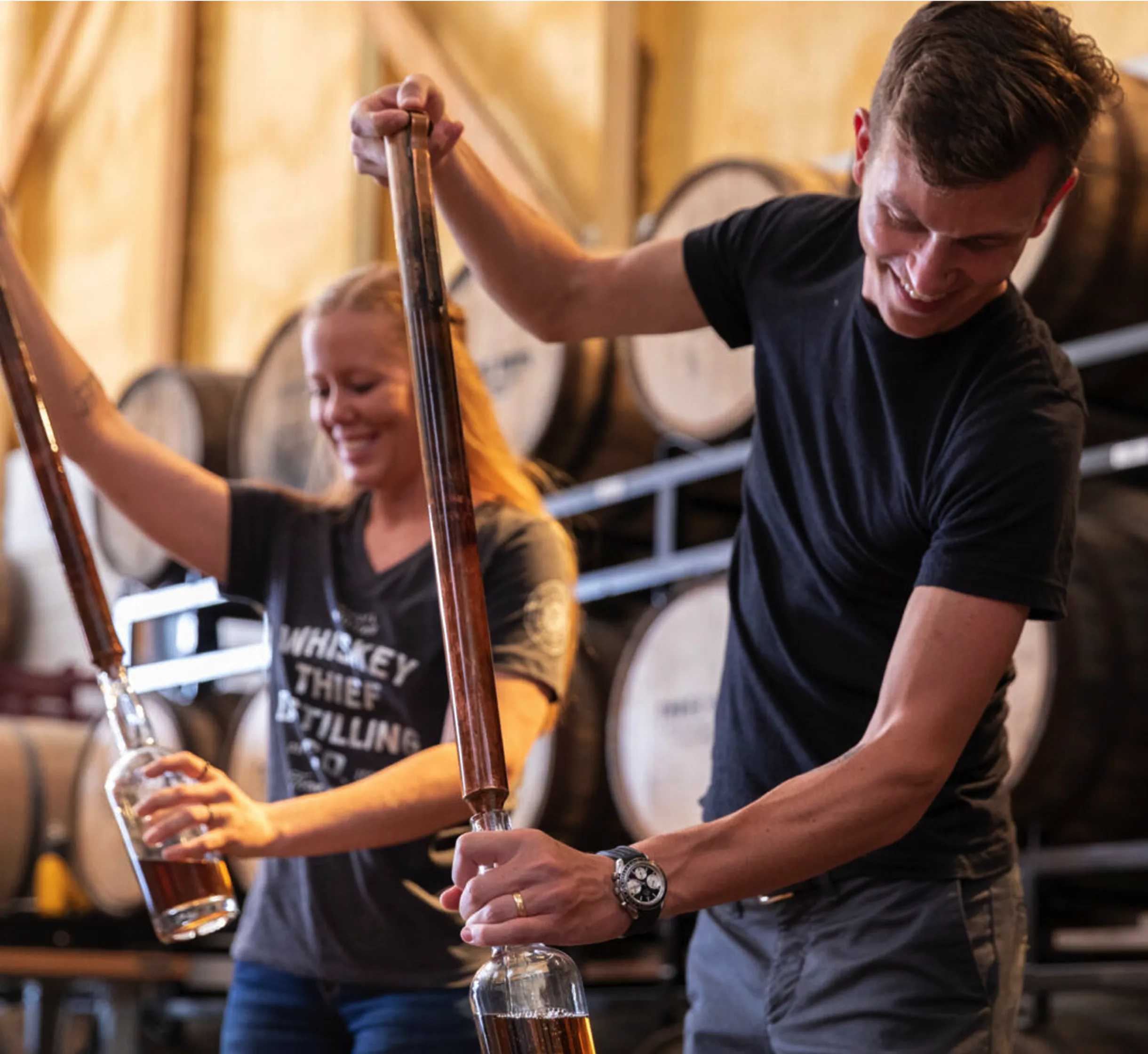 Two happy Whiskey Thief Workers filling bottles using traditional distiller's tool.