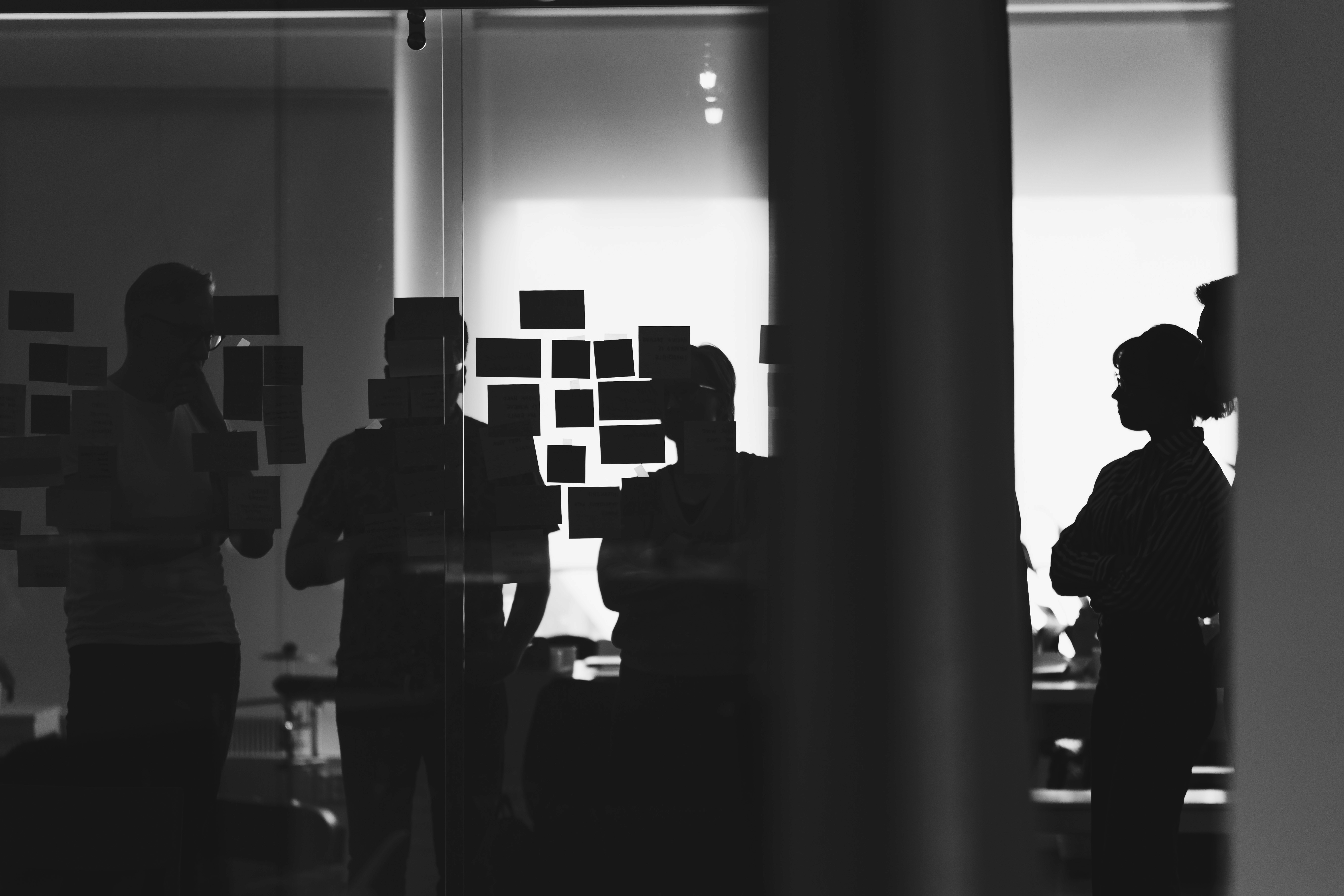 Black and white image of people working at a table with laptops, showing hands gesturing during discussion of digital content displayed on screens, with fabrica® logo in the corner.
