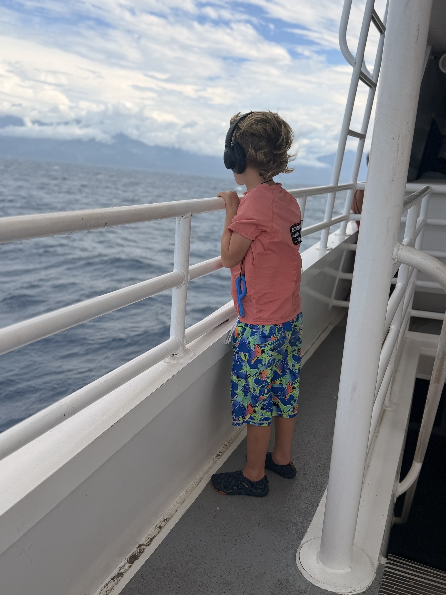 Hyrum on a ferry rail, headphones on, watching the water