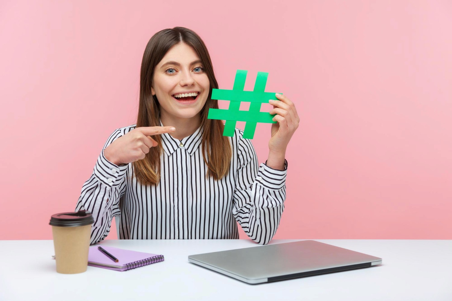 A woman displays a hash sign against a vibrant pink background, emphasizing the symbol's significance in modern communication.