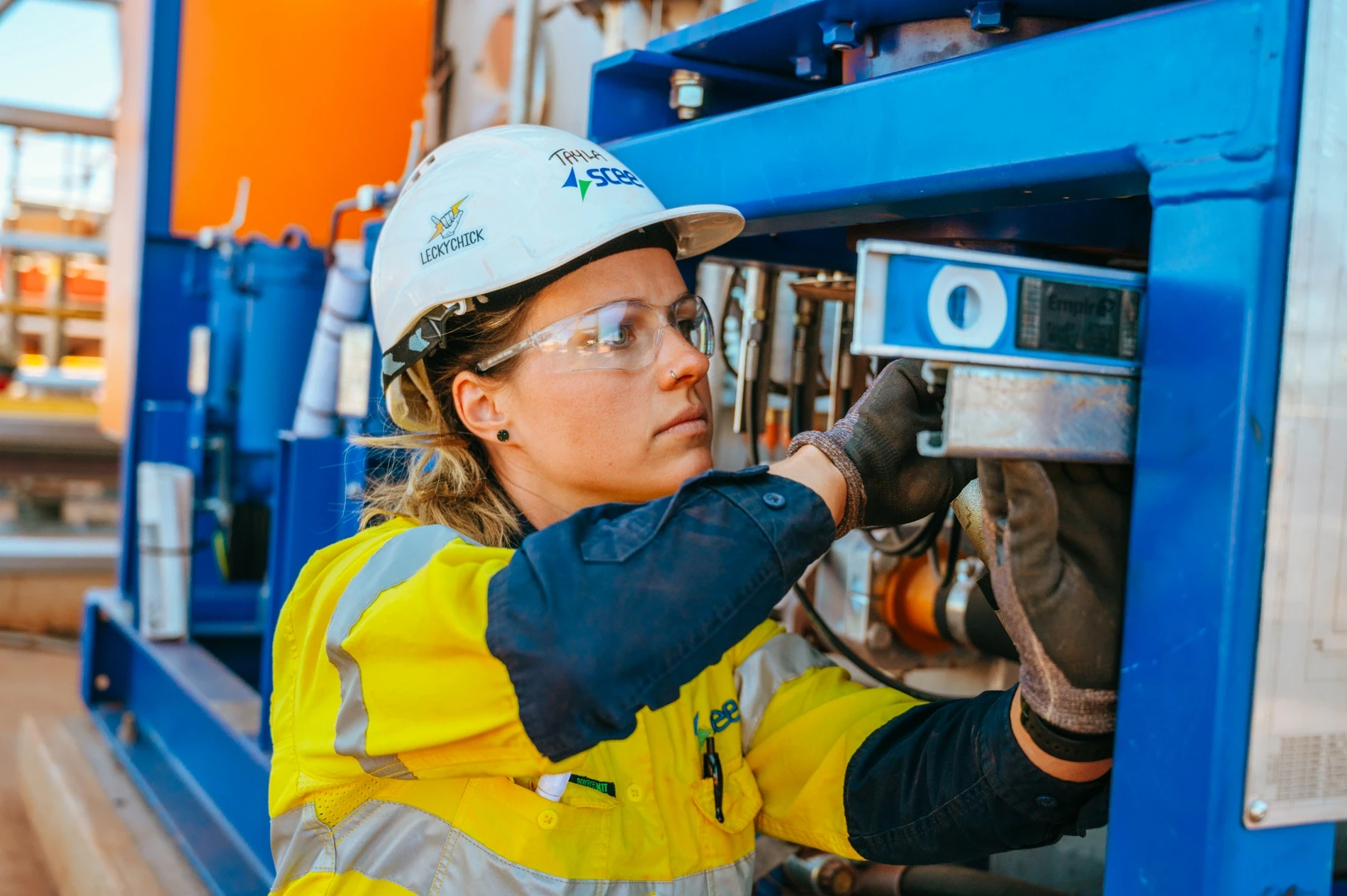 Woman in high-visibility clothing and safety glasses working on blue plant machinery