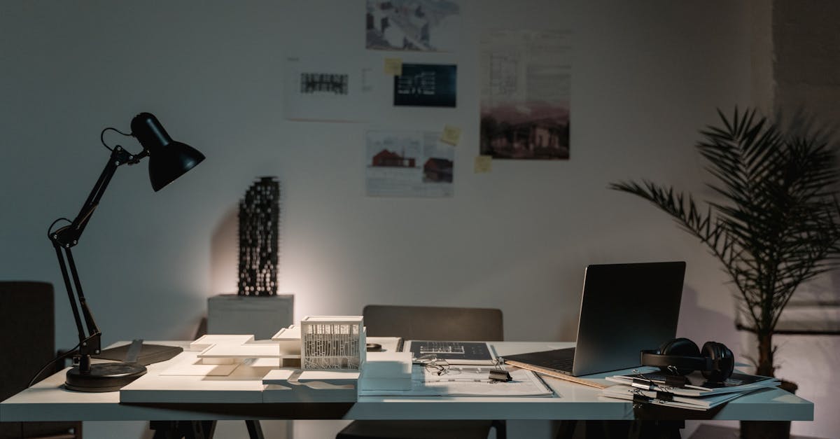 A contemporary architect's desk with design plans, laptop, and lamp in a spacious office.
