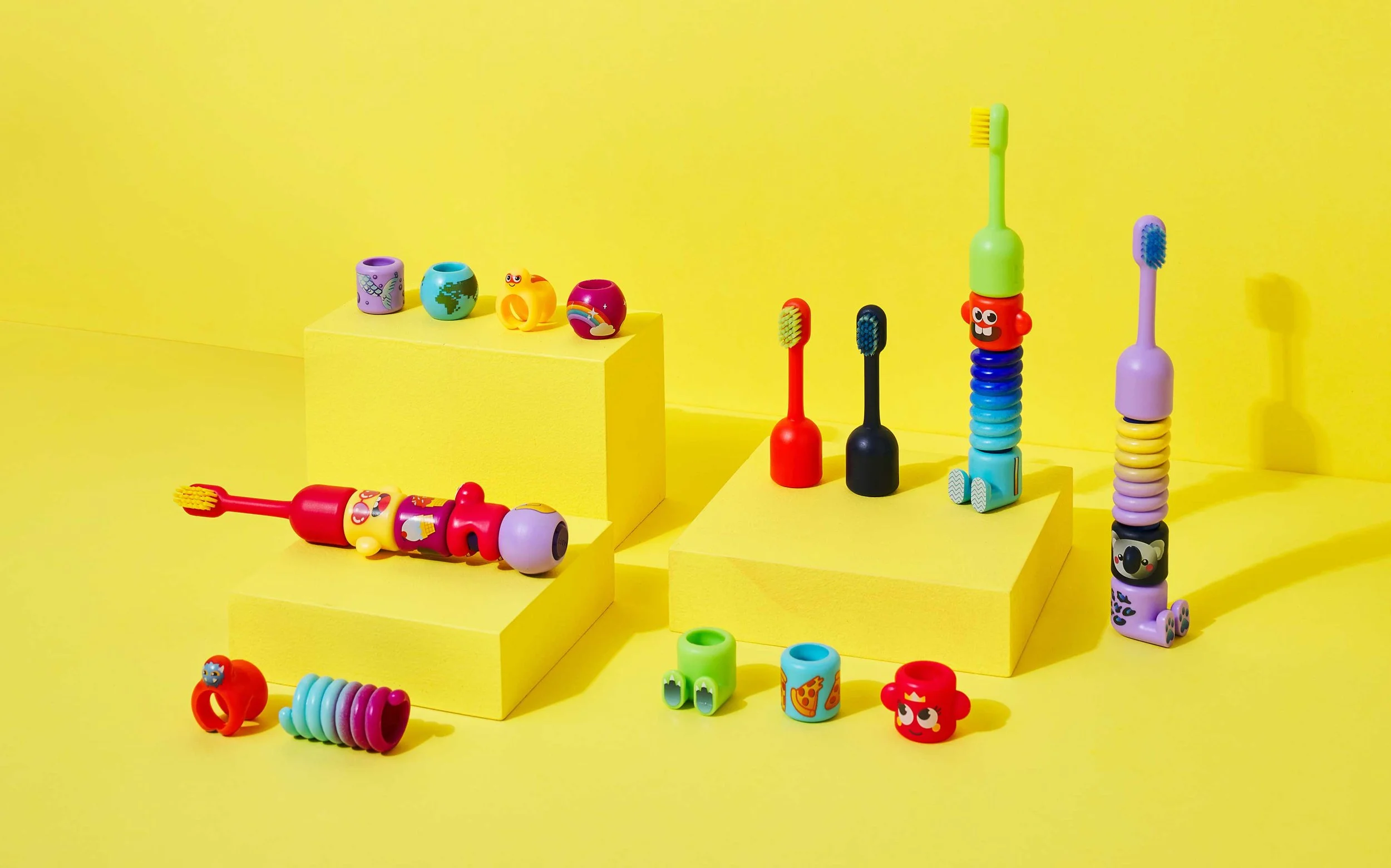 Colorful BABSY Build-A-Brush toothbrushes and interchangeable character pieces arranged on a yellow background