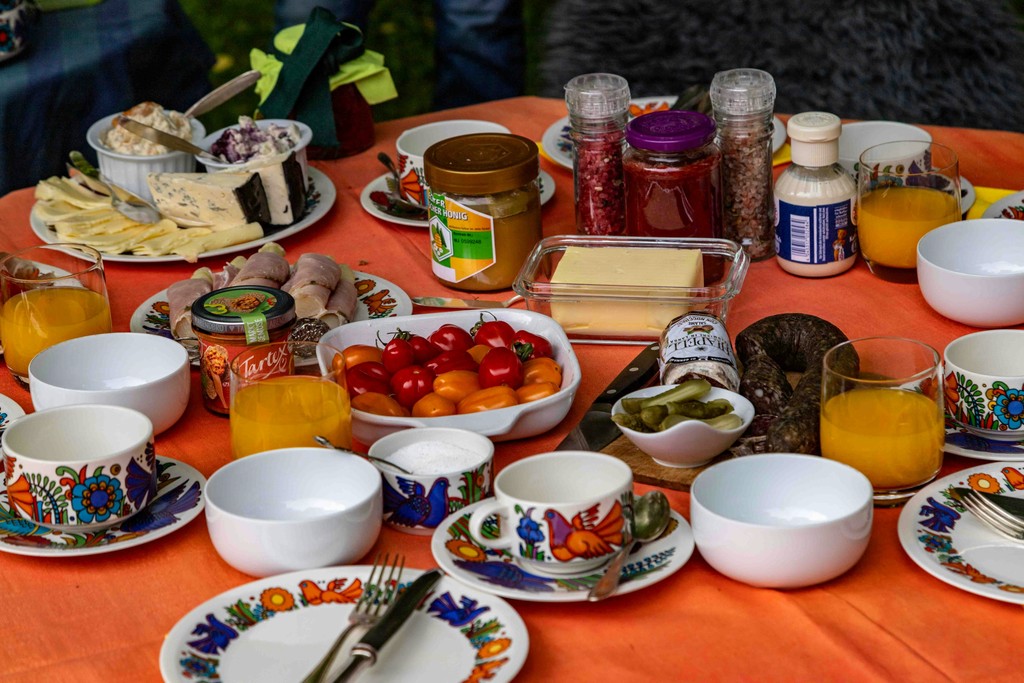 An assortment of healthy, protein-rich snacks including Greek yogurt, nuts, hard-boiled eggs, and protein bars laid out on an orange cloth table.