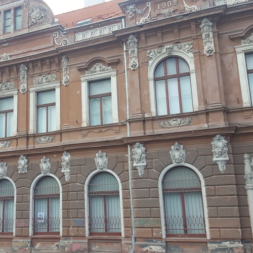アーチ型の窓、装飾的なモールディング、「1902」と刻まれた年が特徴の、華やかな茶色の建物。
