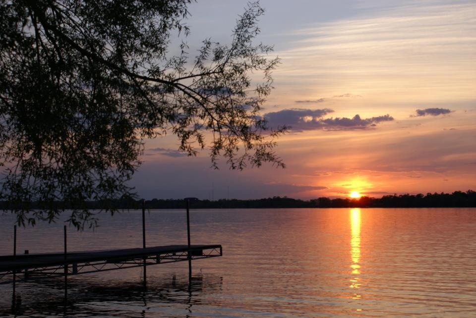 A wooden dock extending into a calm lake at sunset.