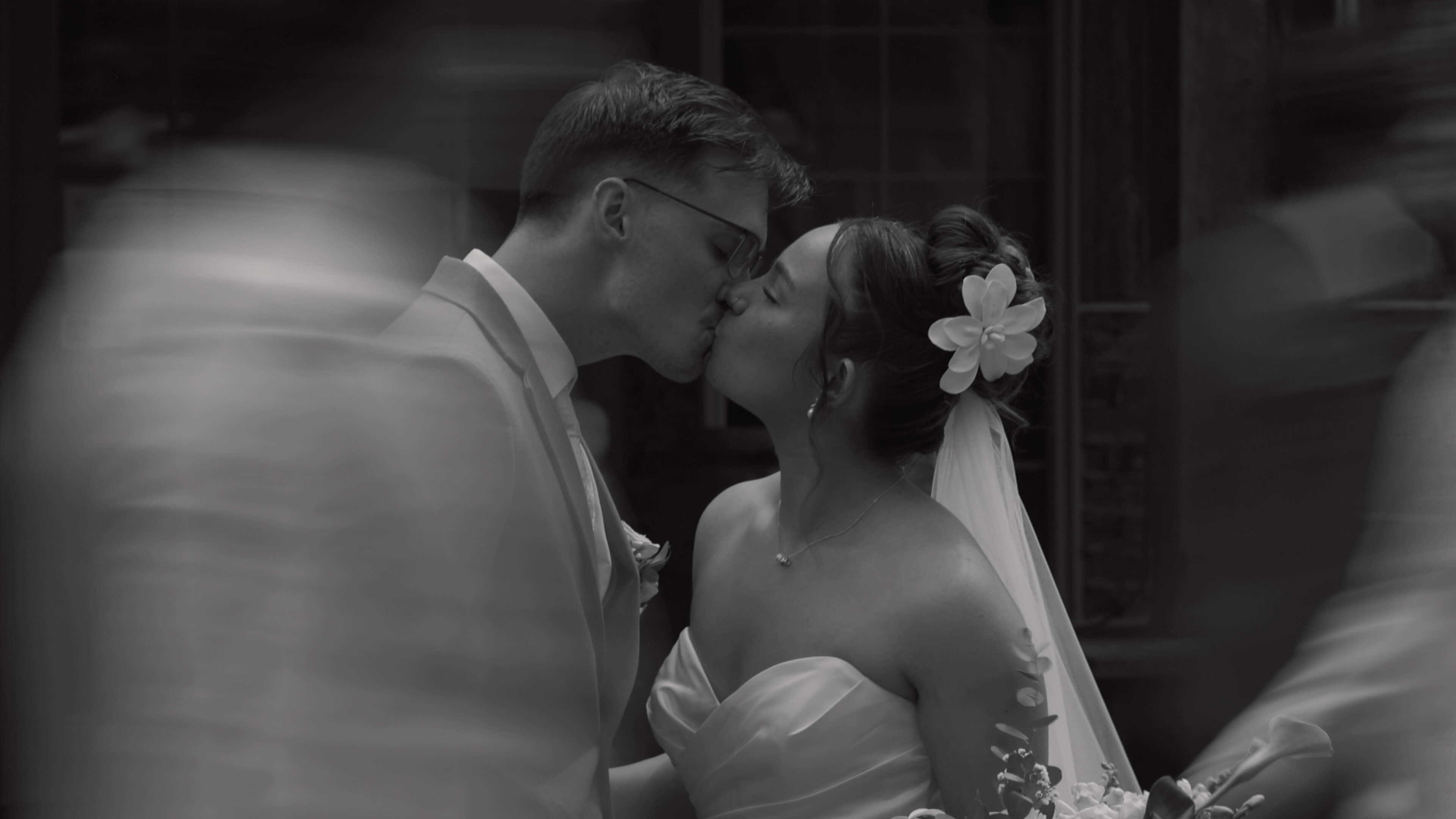 A black and white image of a couple kissing while a blur of people walk around them