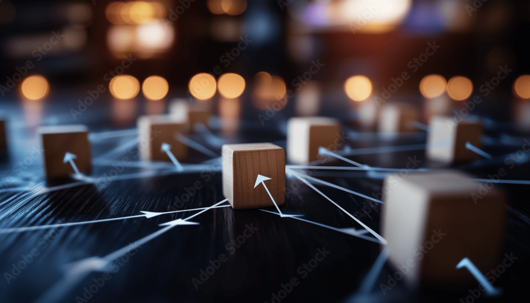 A young person with curly hair smiles at the camera while sitting in front of a laptop against a dark background.
