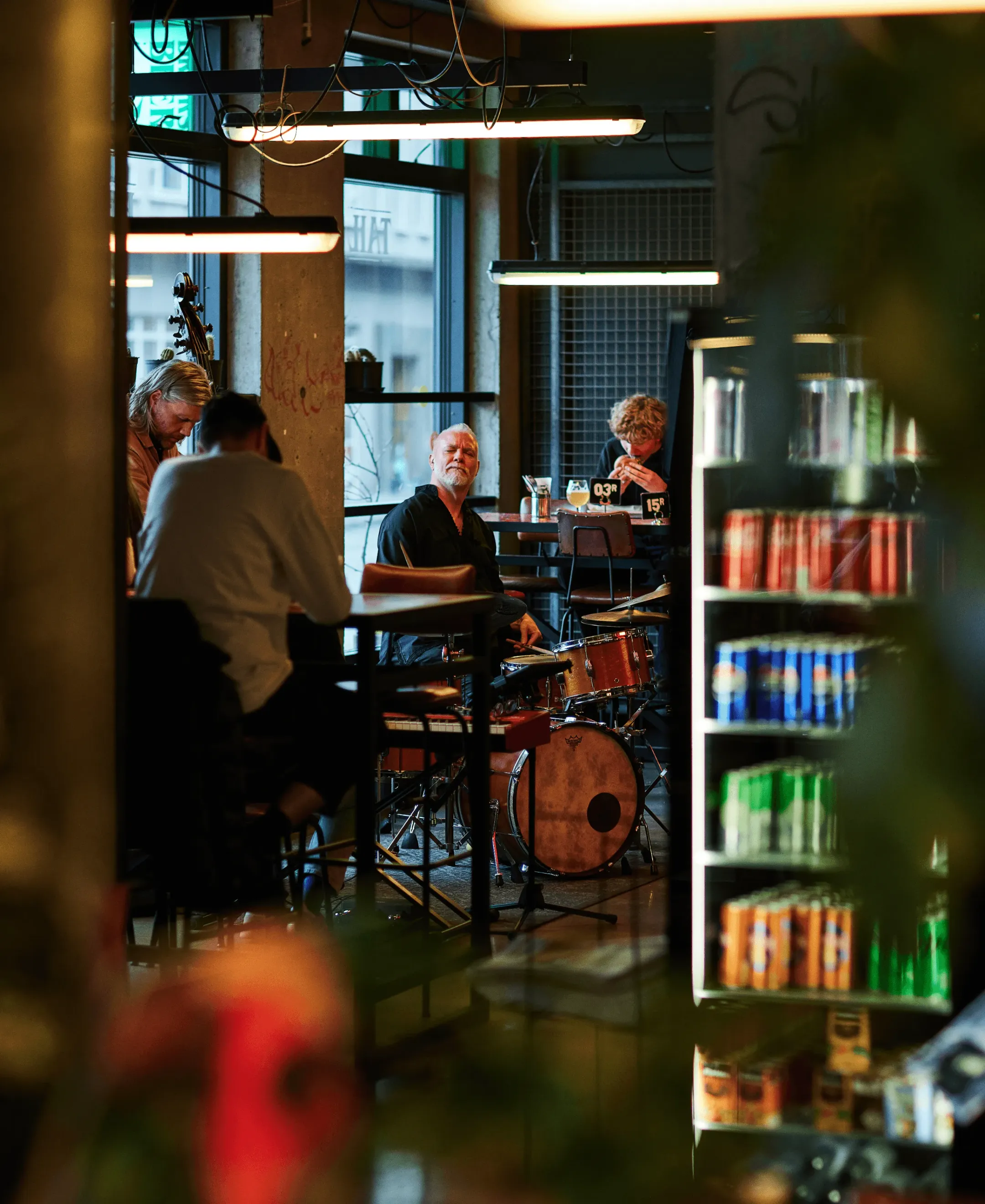 Live band performing indoors beneath colorful lights with audience members nearby