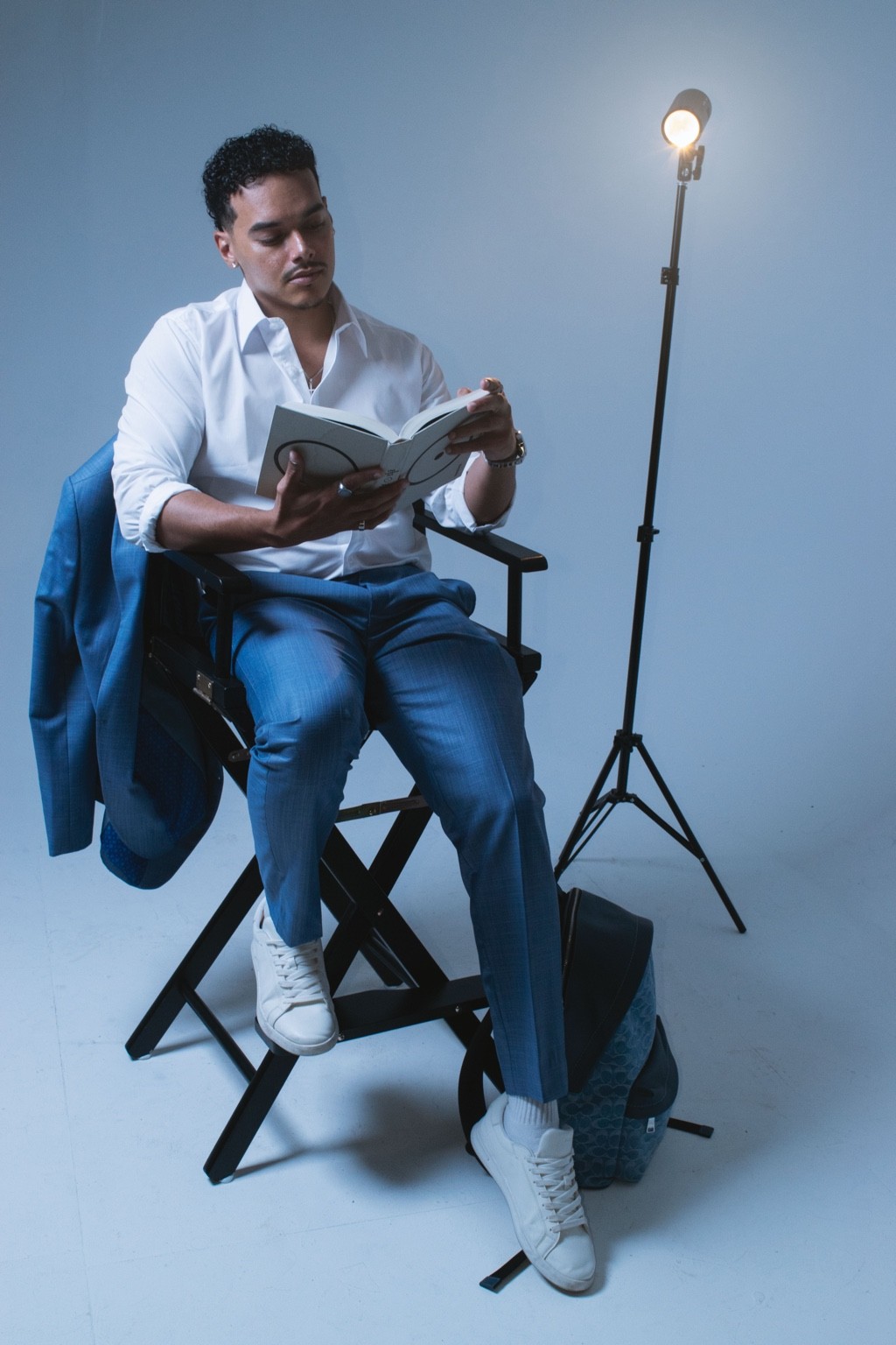 A director’s chair, a book and cool lighting create a relaxed portrait against the white backdrop.