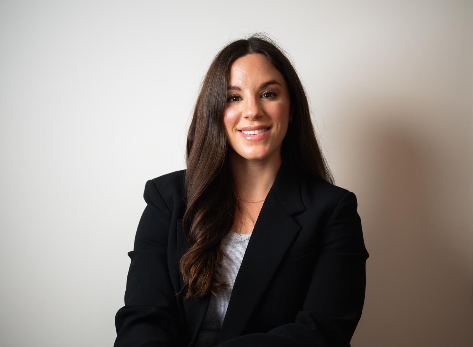 A smiling man with short hair stands with arms crossed, wearing a dark shirt against a neutral background.