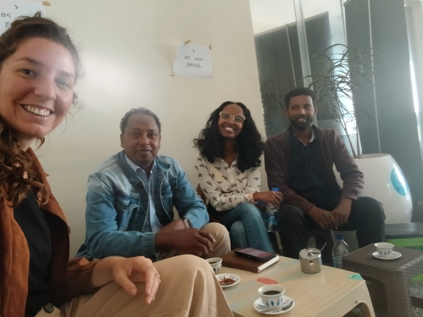 A smiling young man with crossed arms, wearing a plaid shirt and white t-shirt, poses against a dark background.