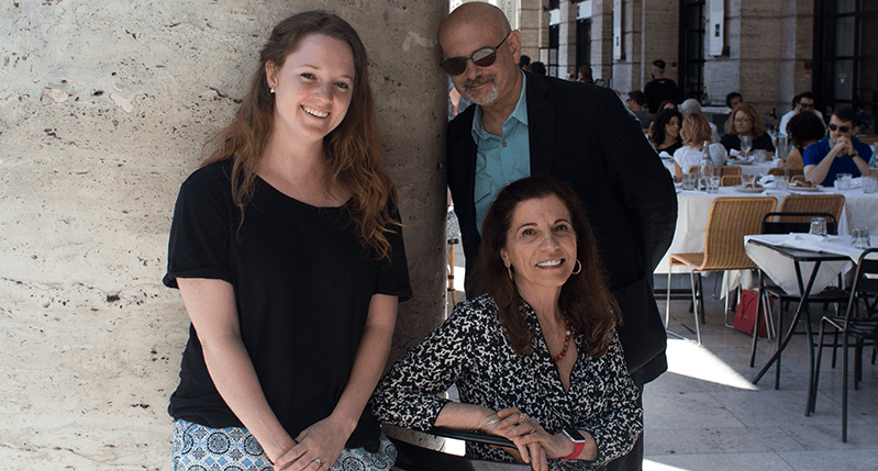 A photo of a man and two women sitting by a stone pillar.