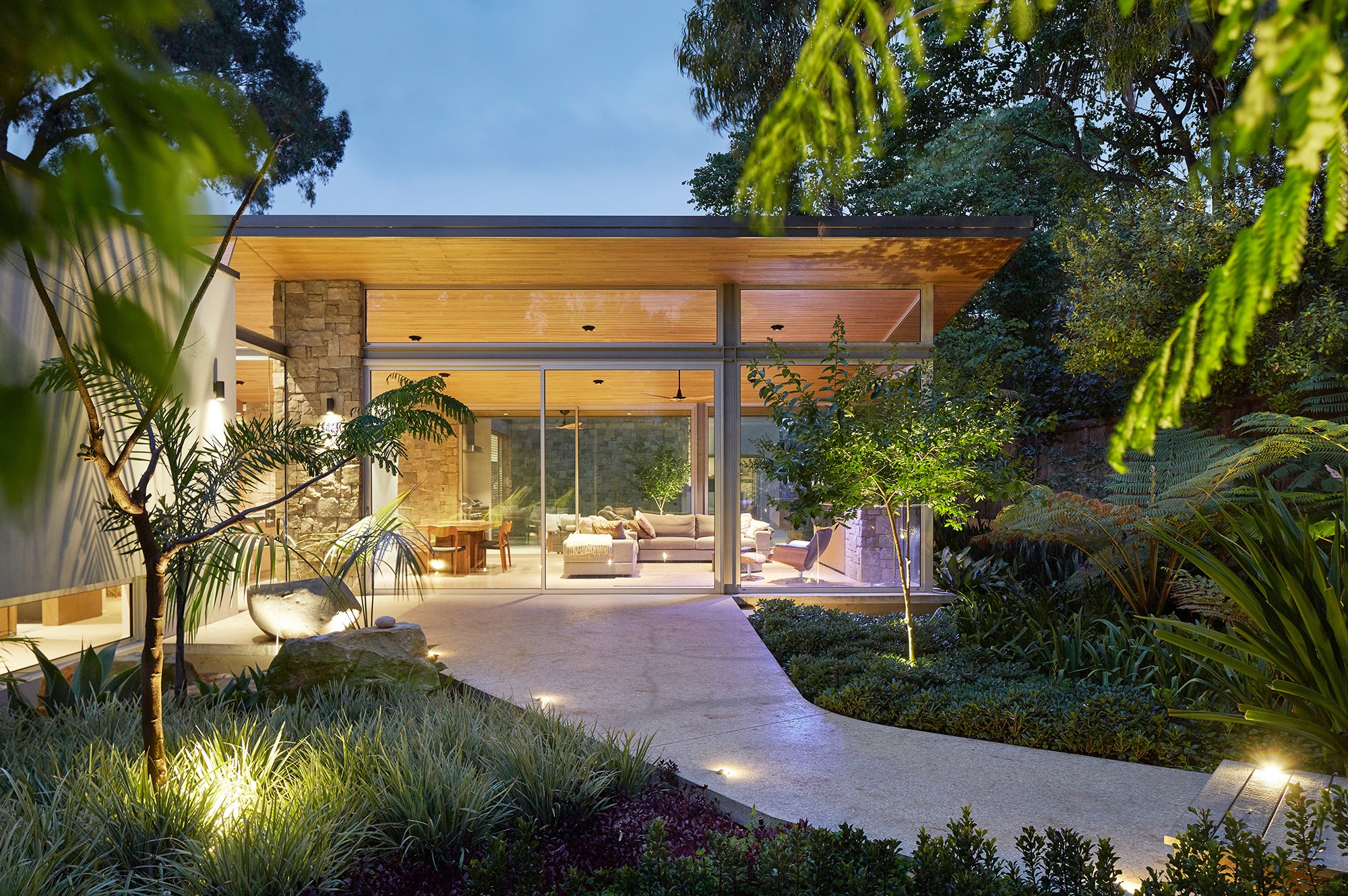 Modern indoor space with large glass doors, lush greenery, and a cozy seating area visible beyond.