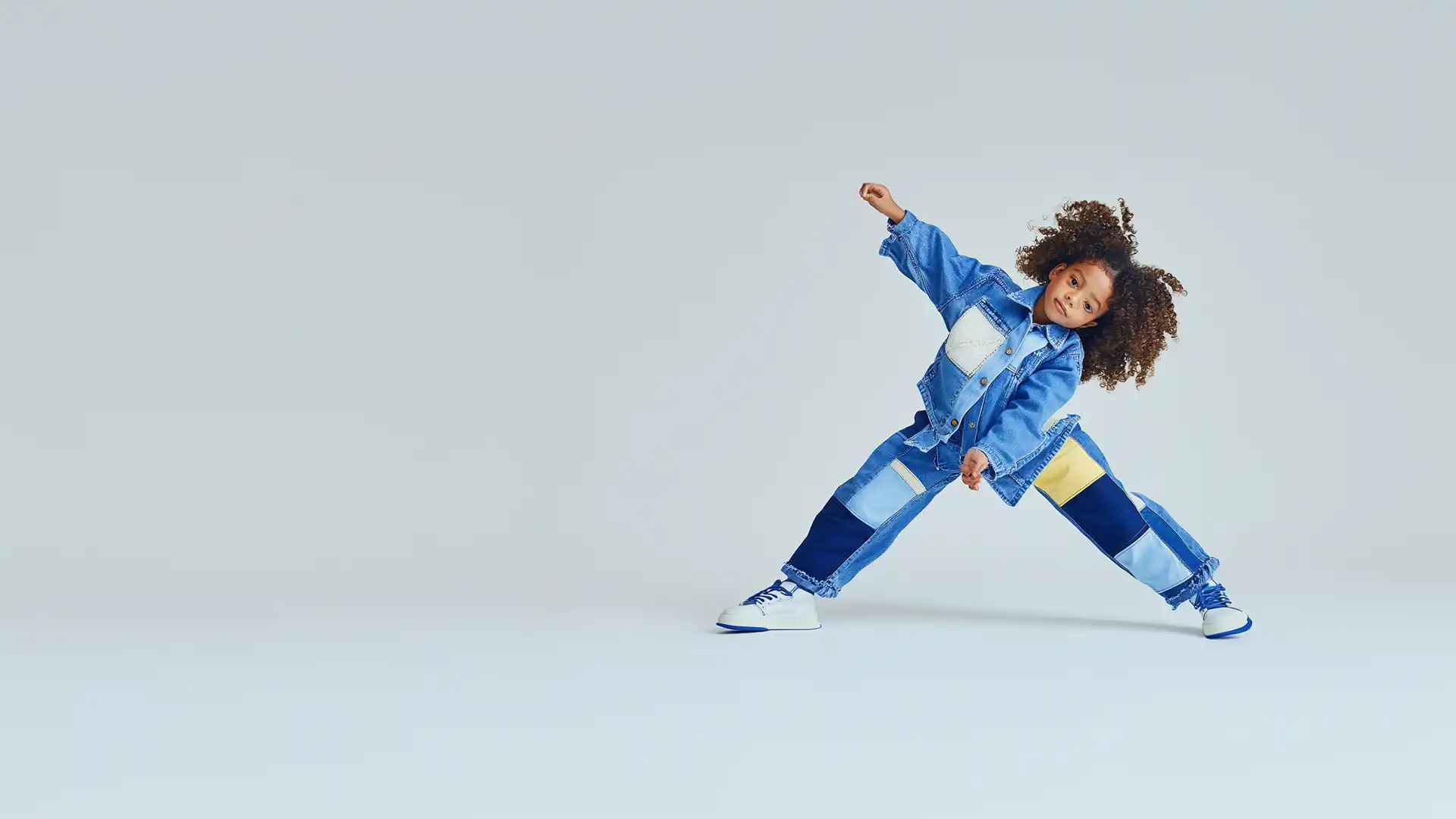 A joyful child striking a playful pose in vibrant denim, symbolizing the dynamic and enriching opportunities in United Nannies’ exceptional network.