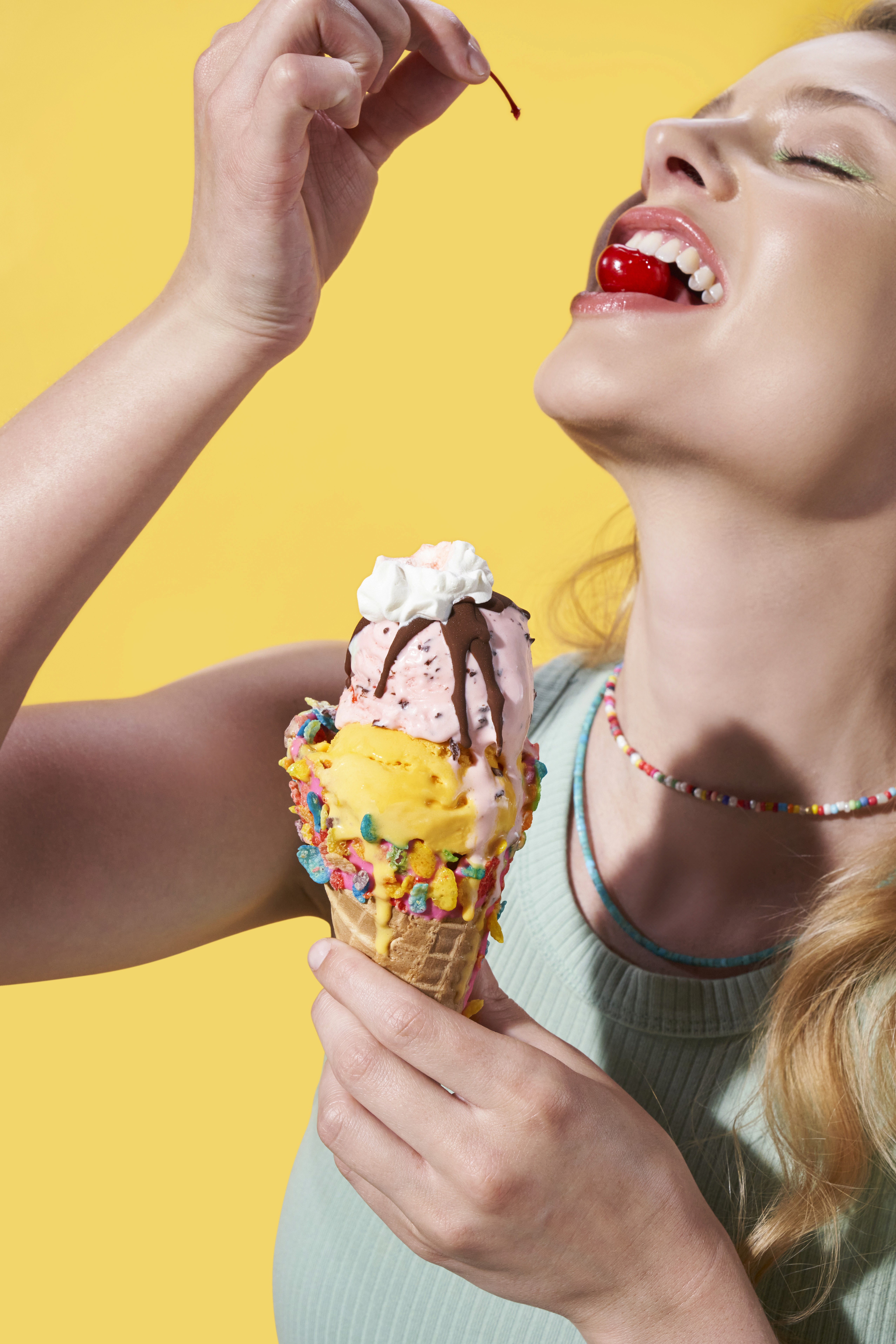 Double scoop ice cream cone held by model eating cherry.