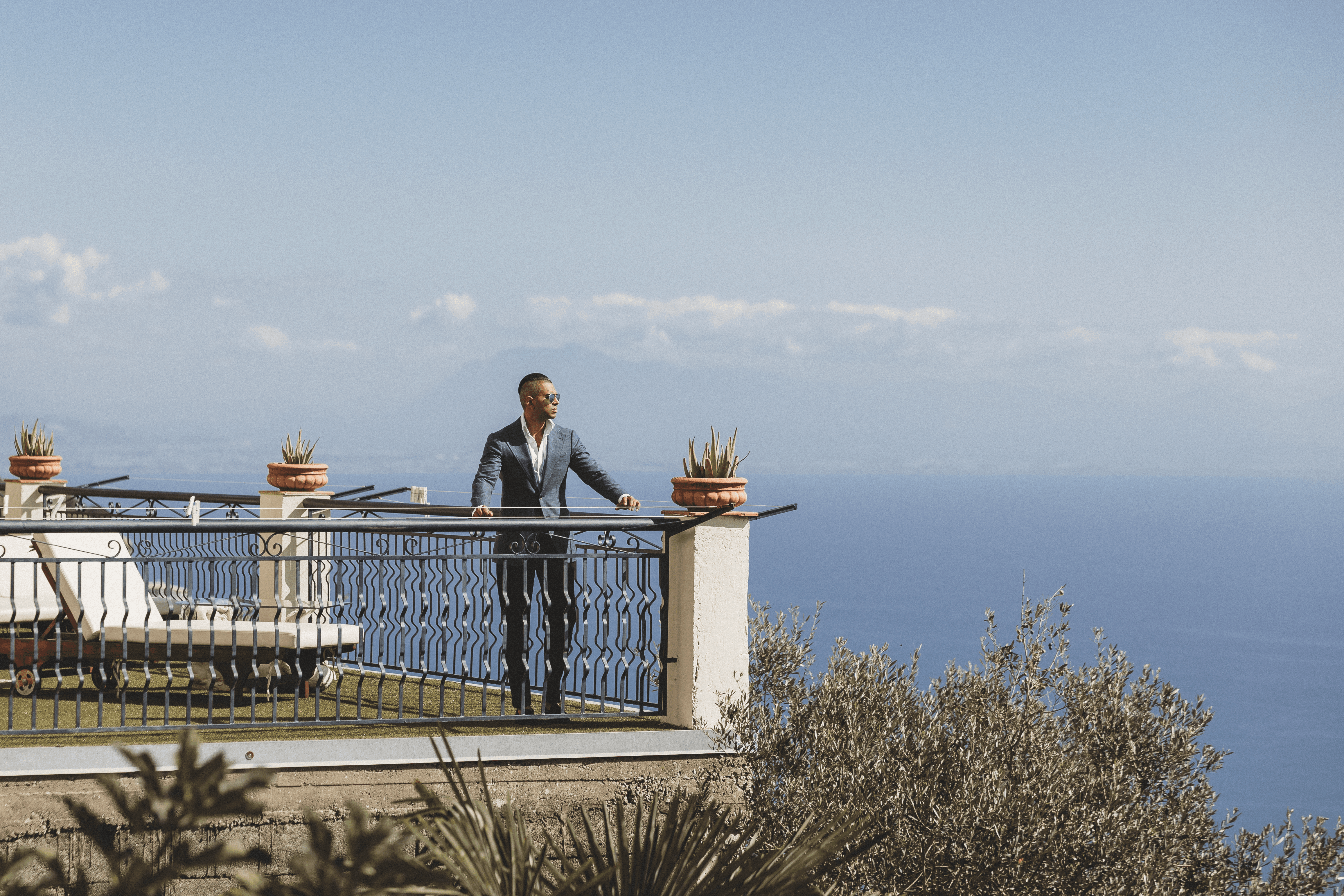 A Don Marrón member stands on a balcony overlooking the Italian coast, wearing a tailored jacket that embodies refinement, craftsmanship, and timeless confidence.