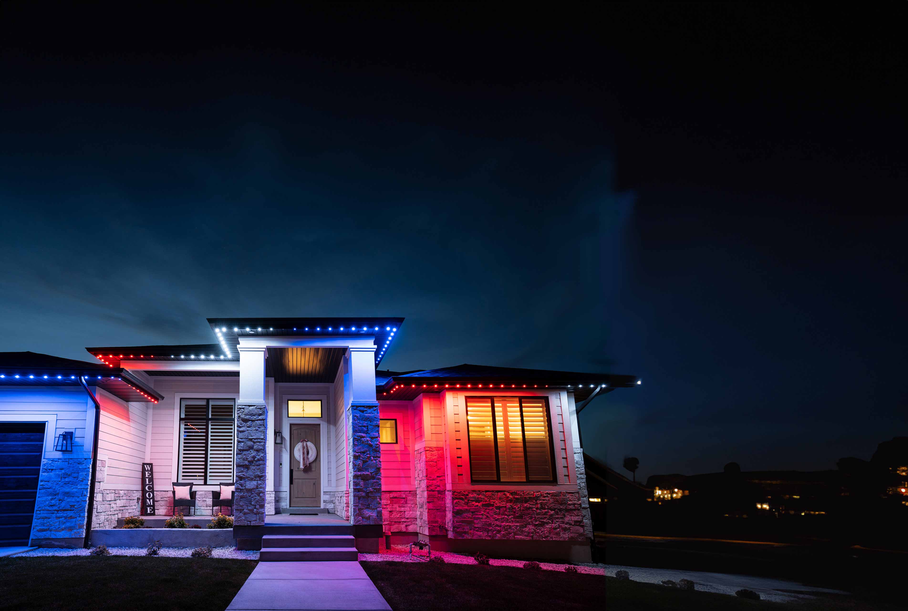 A house at night with white red and green Christmas lighting going along the roof trim