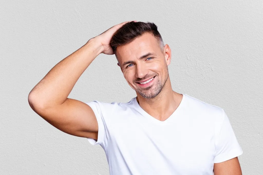 Smiling man touching his hair after PRP restoration treatment, representing non-surgical therapy to stimulate growth and improve hair thickness.