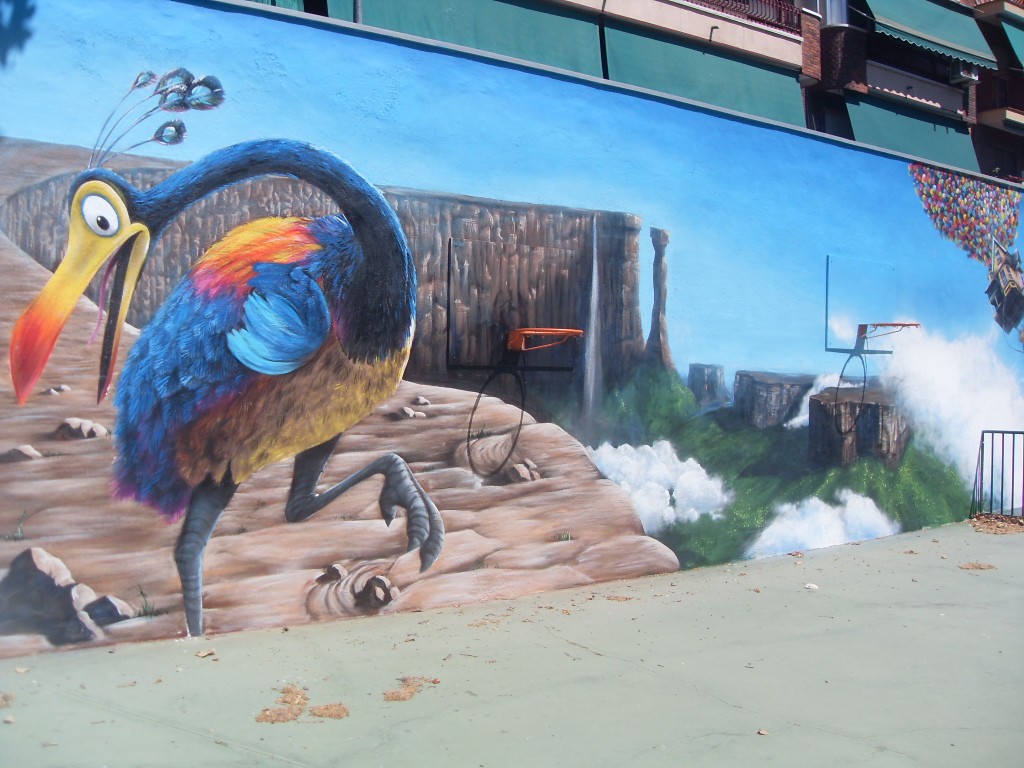 Mural pintado a mano de un ave exótica de plumaje azul, naranja y amarillo en la fachada de un recinto exterior.