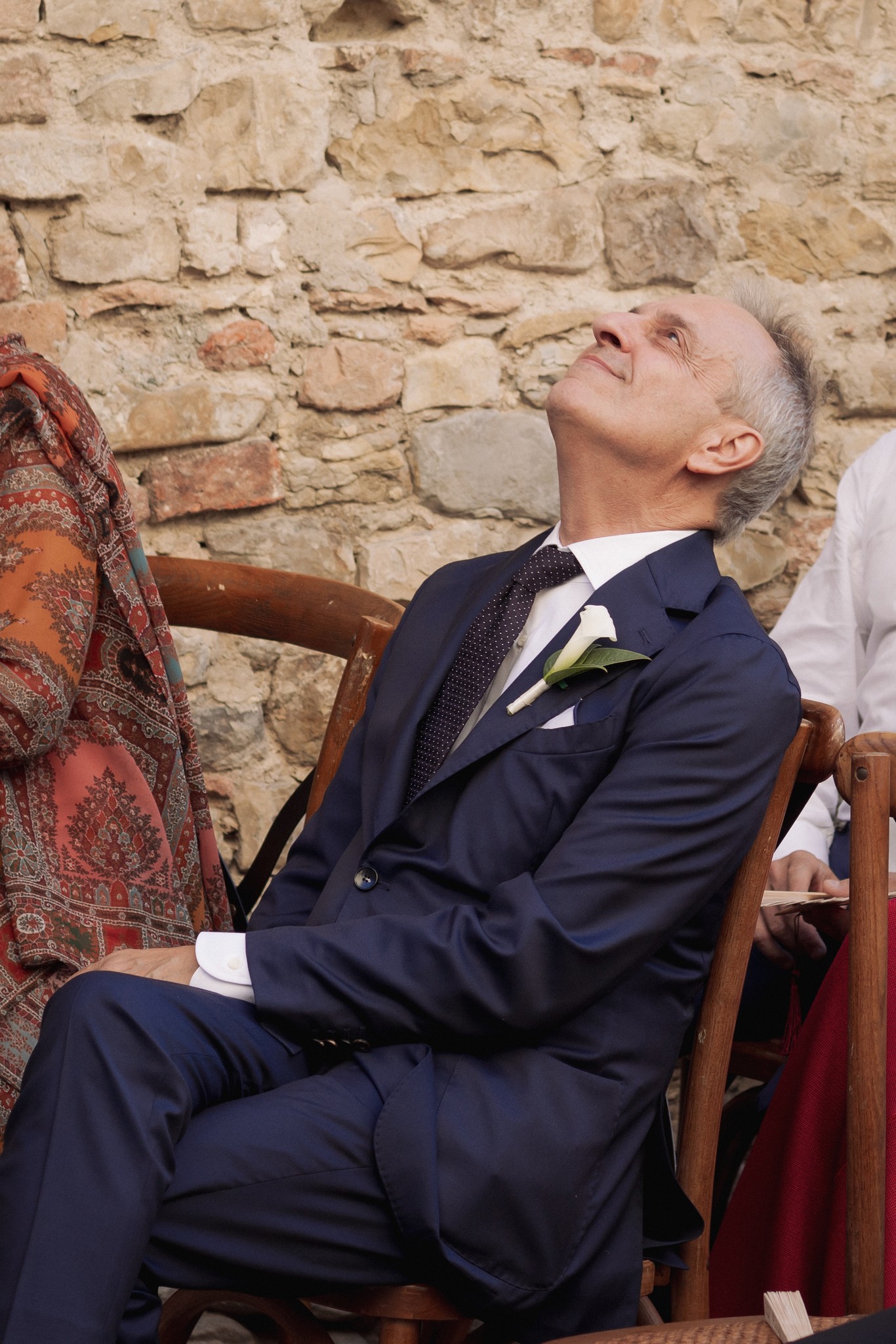 Sposo in abito blu seduto con volto rivolto, muro pietra Castello Scipione durante cerimonia matrimoniale