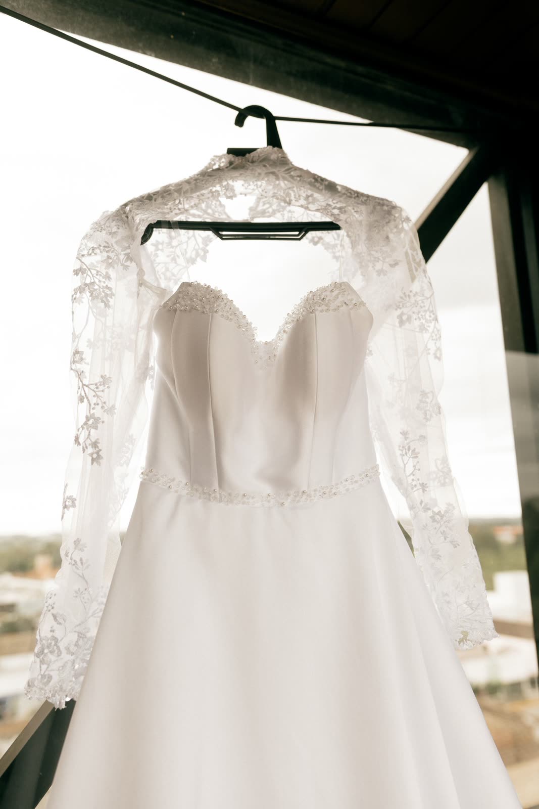 Lace-shouldered wedding dress on a hanger by a bright window