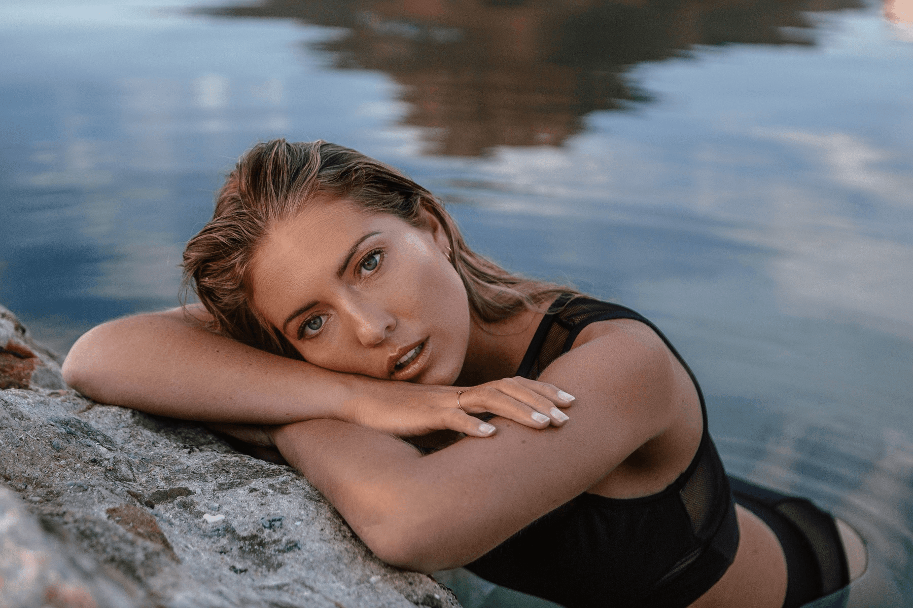 Micharn Pollock resting on a rock in shallow water wearing a black swimsuit.