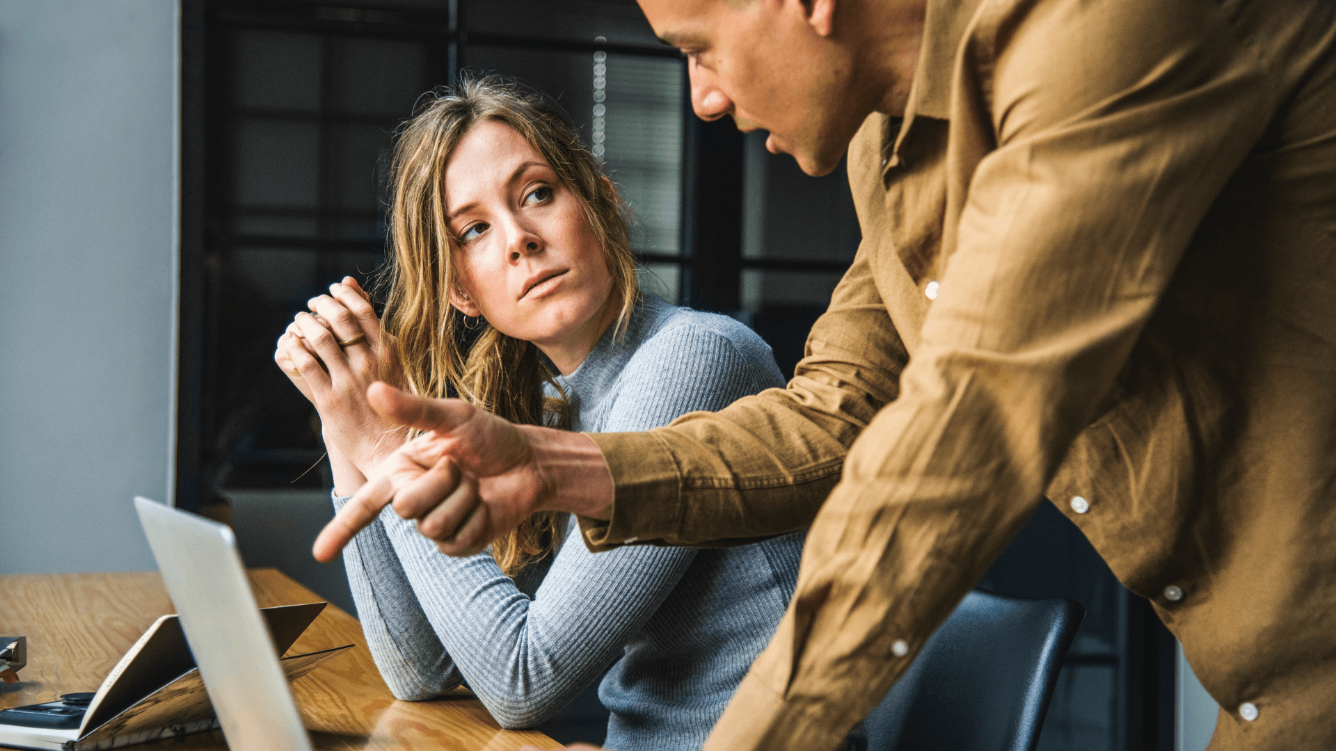A woman sitting down while another person leans over an indicates something on a laptop screen