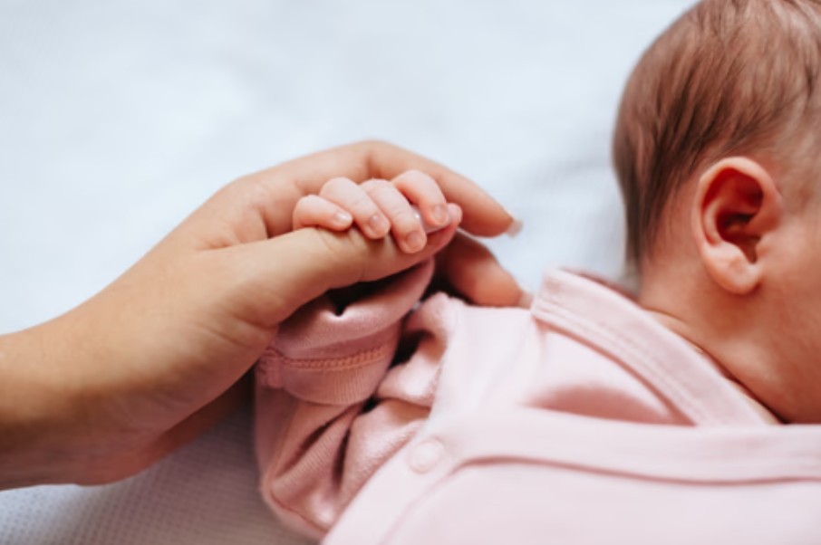 Newborn baby's hand wrapped around the thumb of her mother, a great idea for a baby photo book..