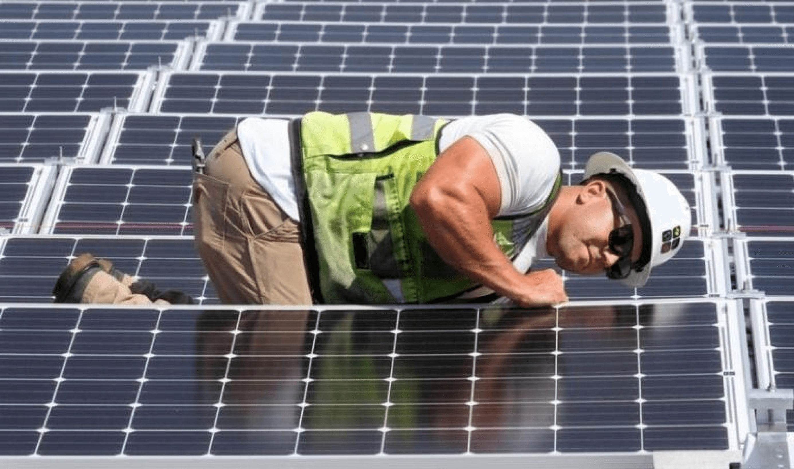 A worker in a safety vest and helmet inspects solar panels on a rooftop.