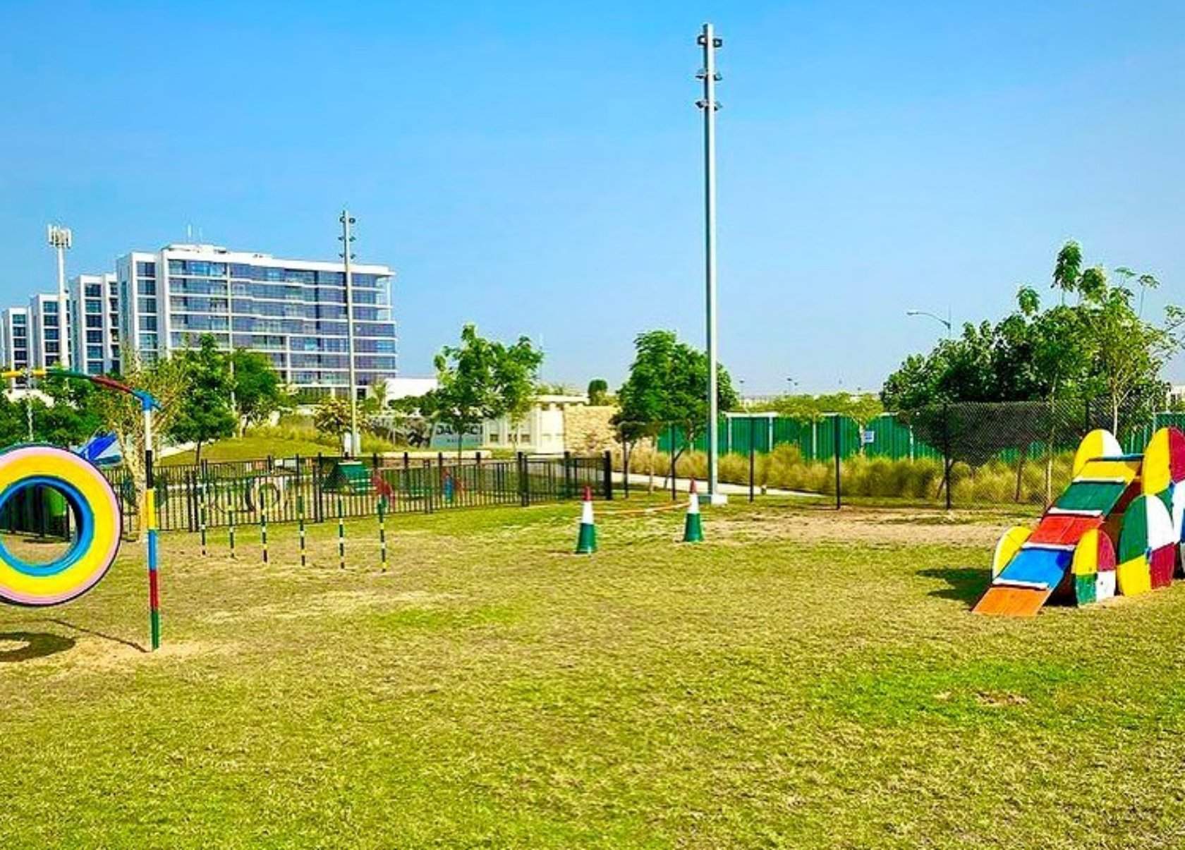 The Damac Hills Dog Park with colorful agility training equipment, fences, and a backdrop of the city.
