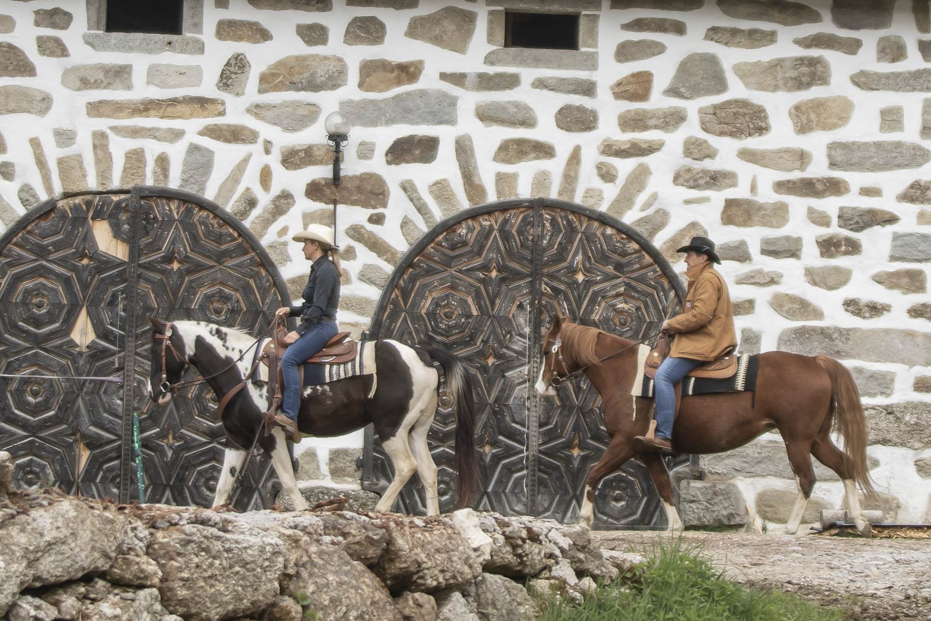Pferde in Wanderreitausrüstung grasen auf einer Wiese neben ihren Reitern im Hochland. Im Hintergrund ein weiter Ausblick und Windmühlen.
