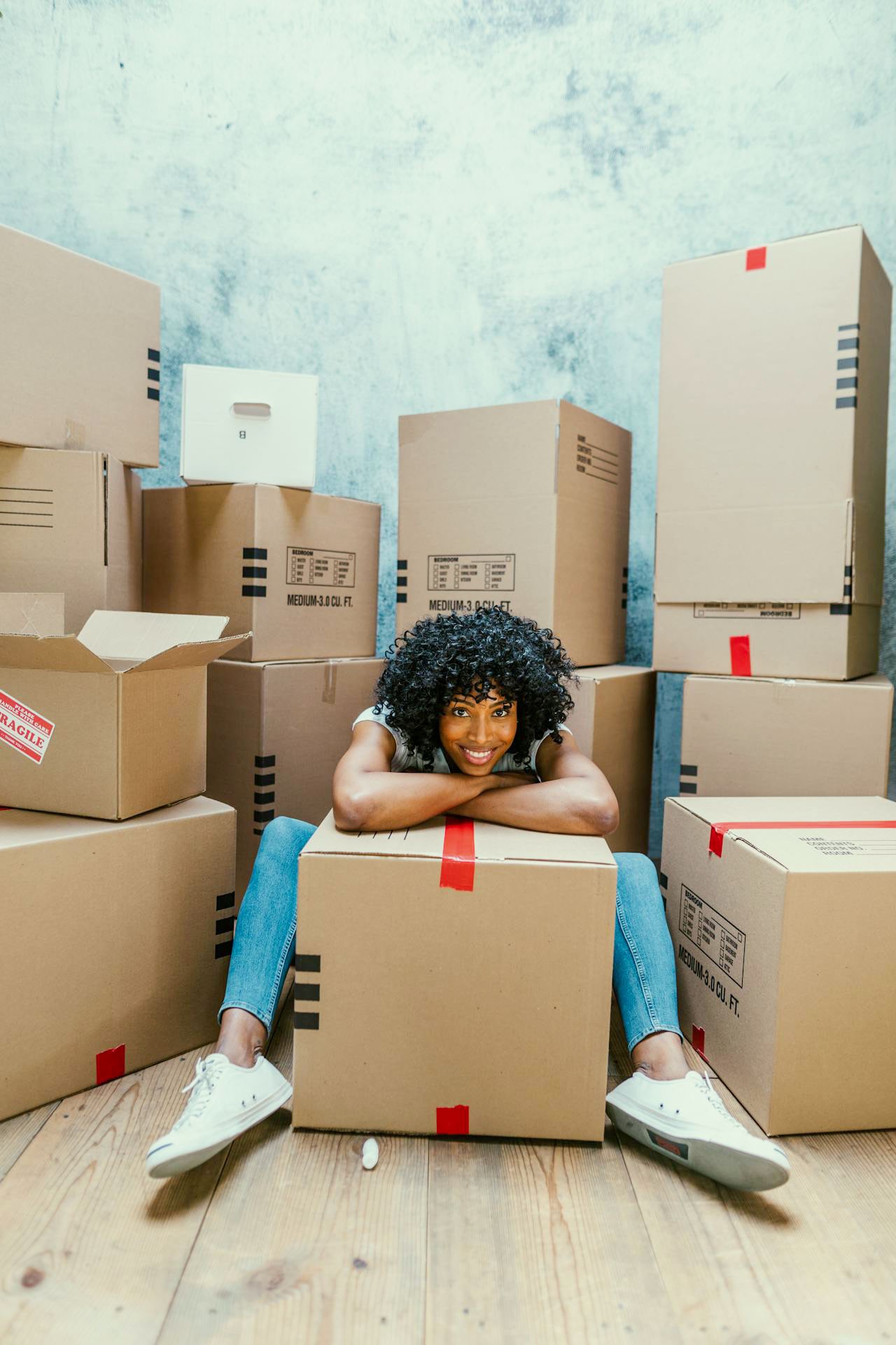 Woman with lots of boexes around her, smiling to the camera.