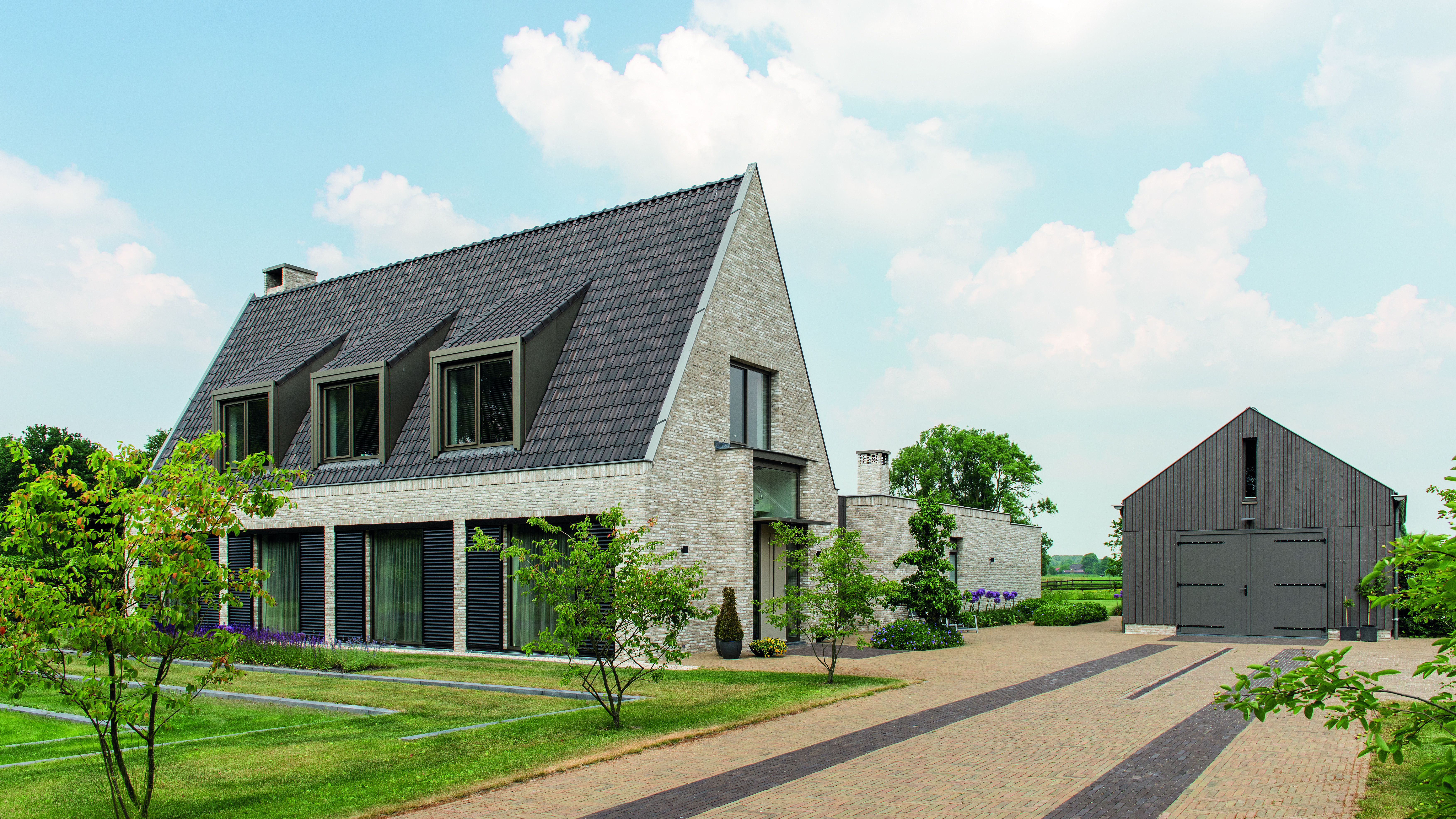 Moderne woning met strakke lijnen, oprit en bijgebouw op zonnige dag.