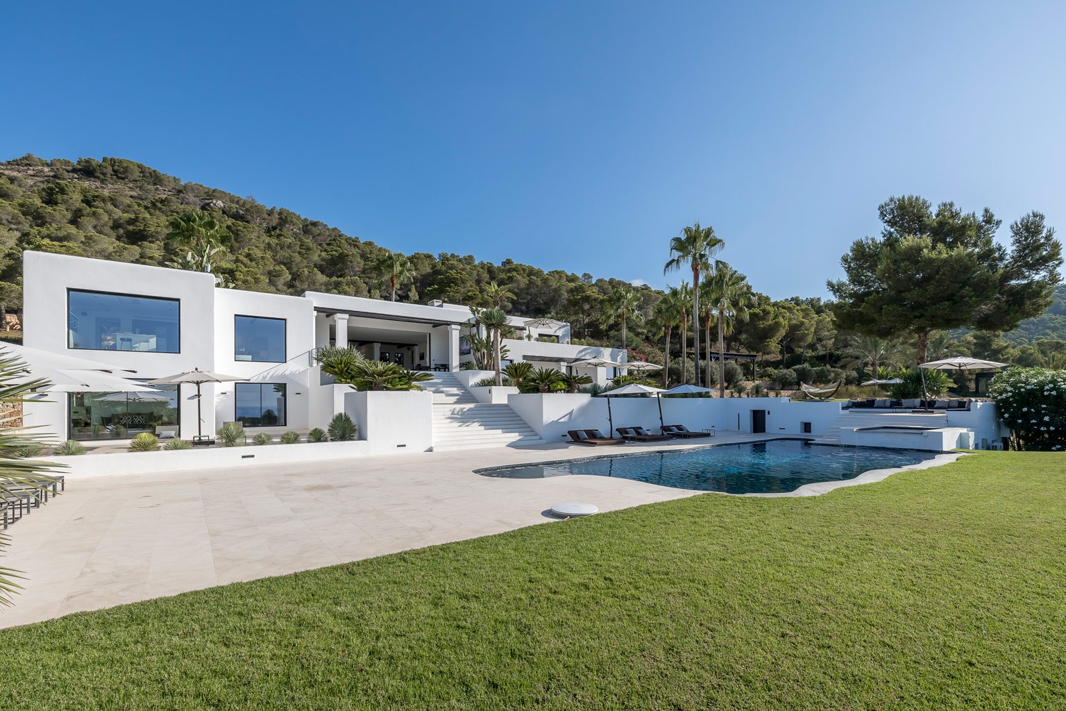 Luxury white Ibiza villa with pool, sun terraces and landscaped gardens set against green hillside in Cap Martinet.